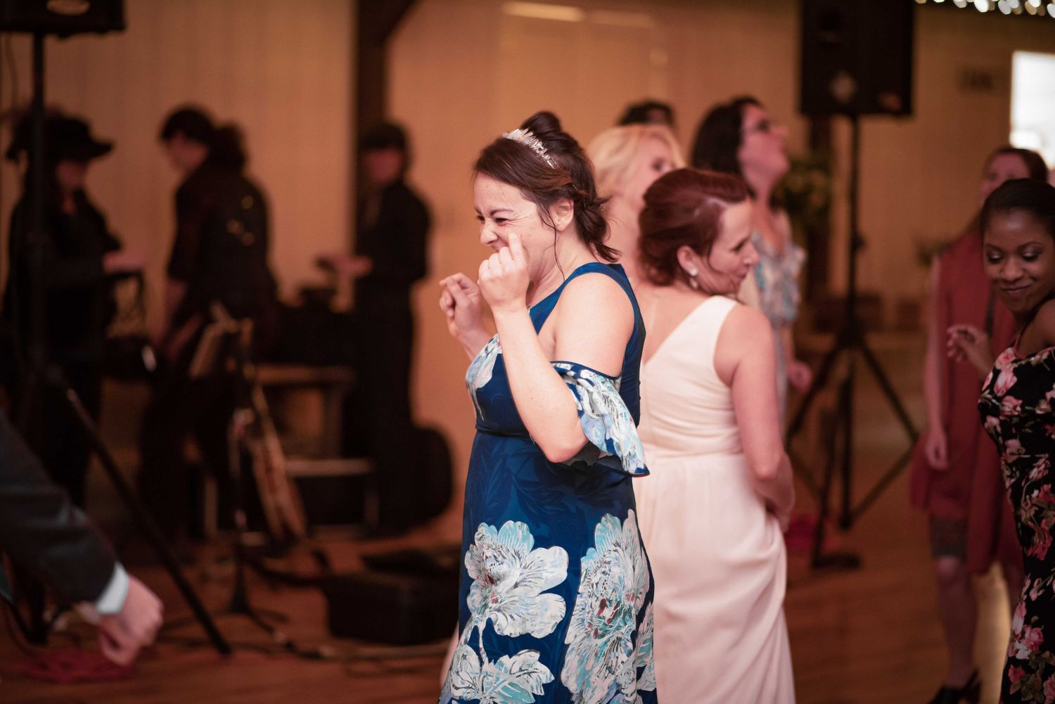 Guests dancing and laughing at a wedding reception with a live band performing in the background.
