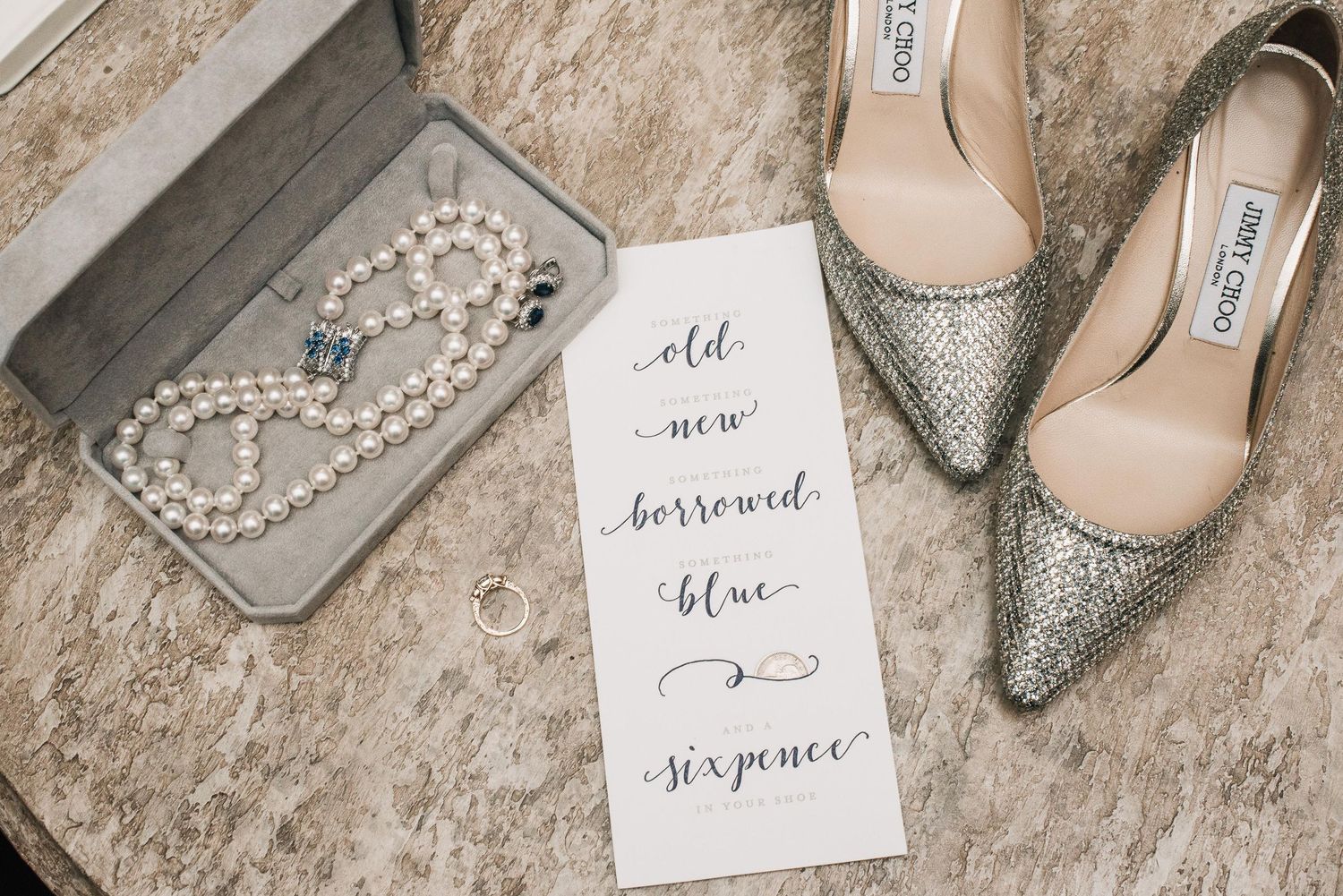 Pearl necklace, gold rings, Jimmy Choo glitter heels, and an old new borrowed blue sixpence wedding card on marble.