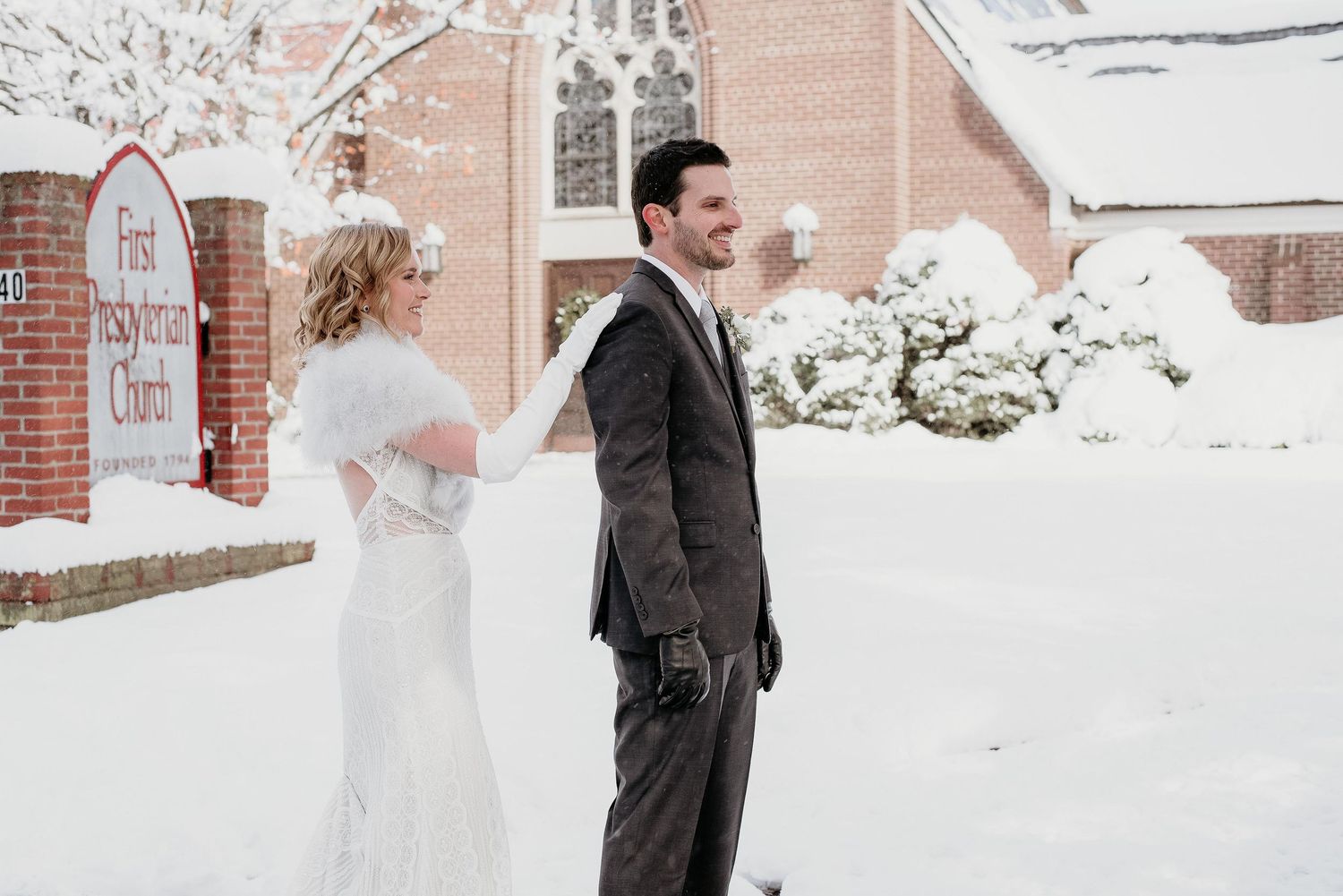 Bride and groom share a romantic moment outside First Presbyterian Church in a snowy winter wedding setting.