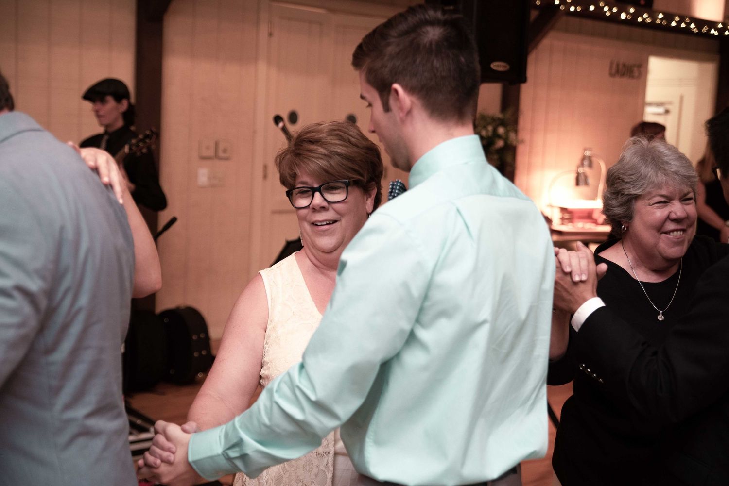 Guests dancing at a wedding reception, woman in pink dress dancing with man in mint green shirt.