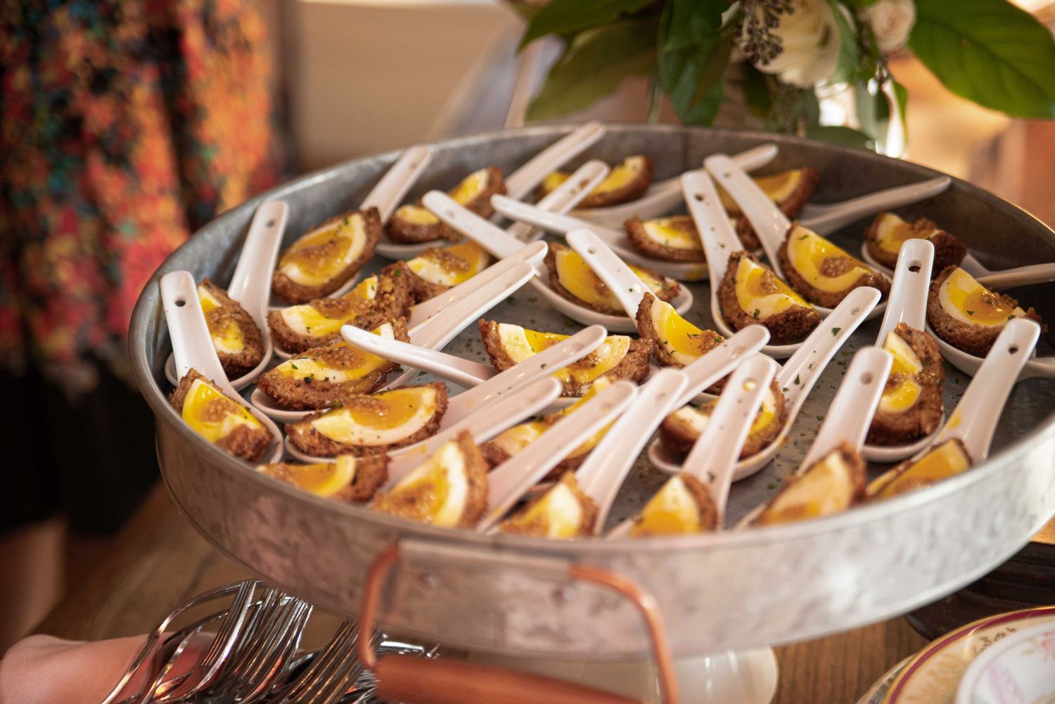 A large silver pan filled with roasted fruit slices served on individual wooden spoons at a catered event.