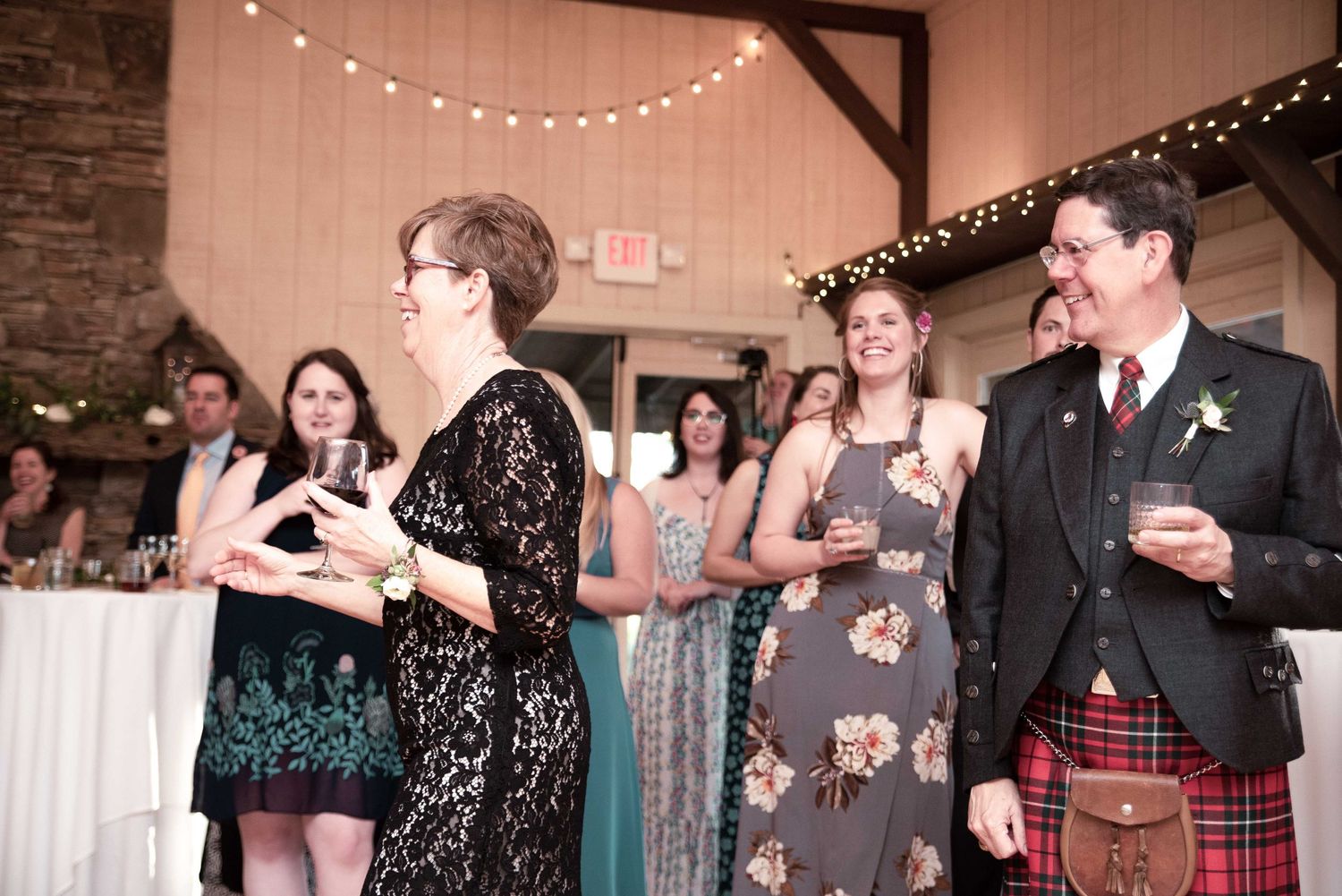 Guests laughing and socializing at a wedding reception, man in Scottish kilt holding a drink.