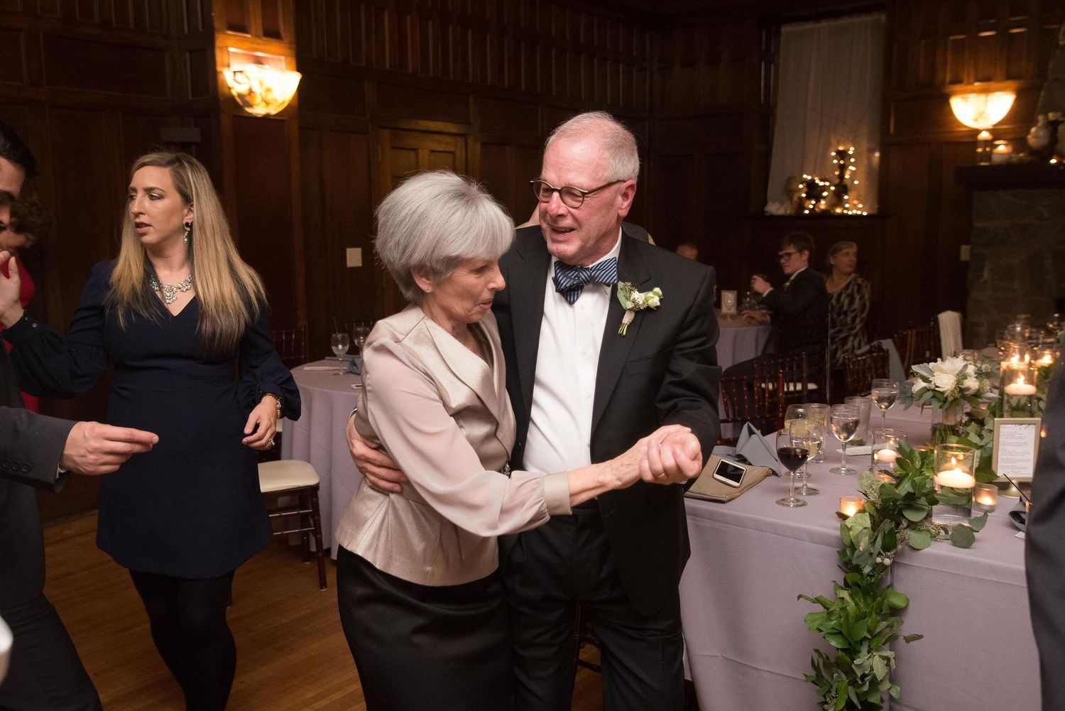 Elderly couple dancing elegantly at a wedding reception in a warmly lit venue with floral decorations.