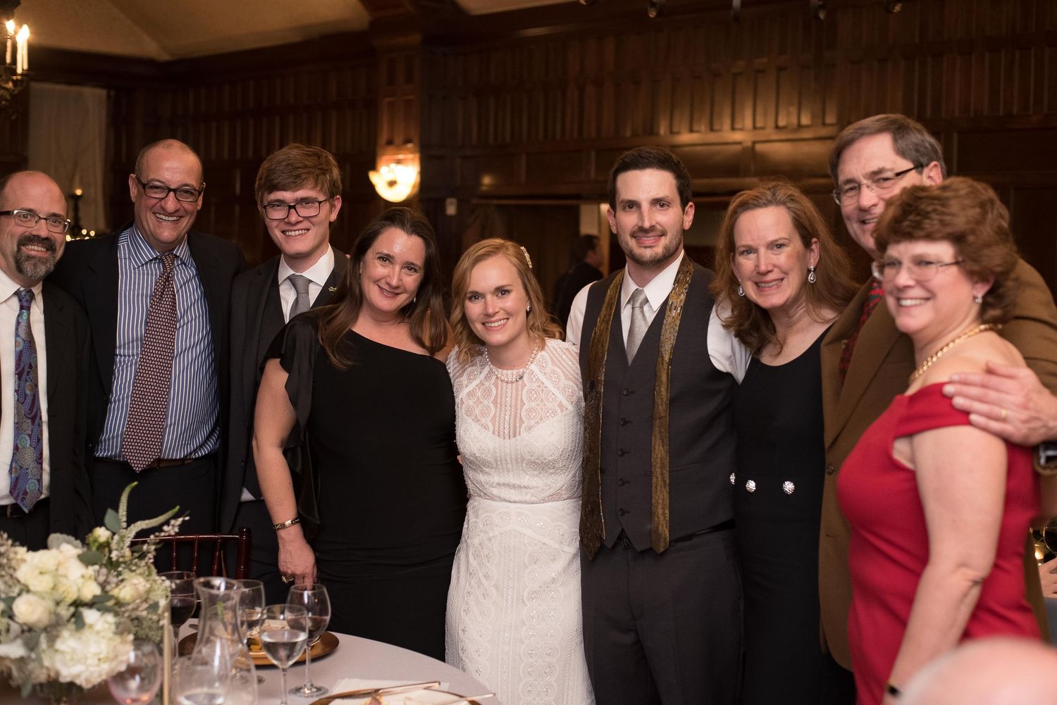 Group of nine people posing together at a wedding reception, bride and groom in center.