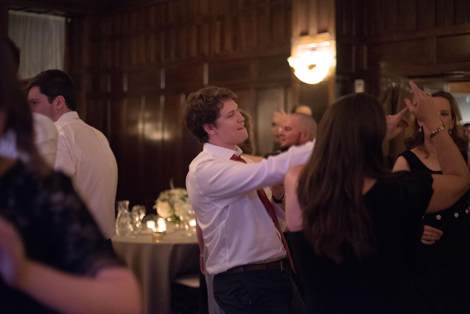 People dancing and socializing at an elegant evening party in a dimly lit wood-paneled venue.