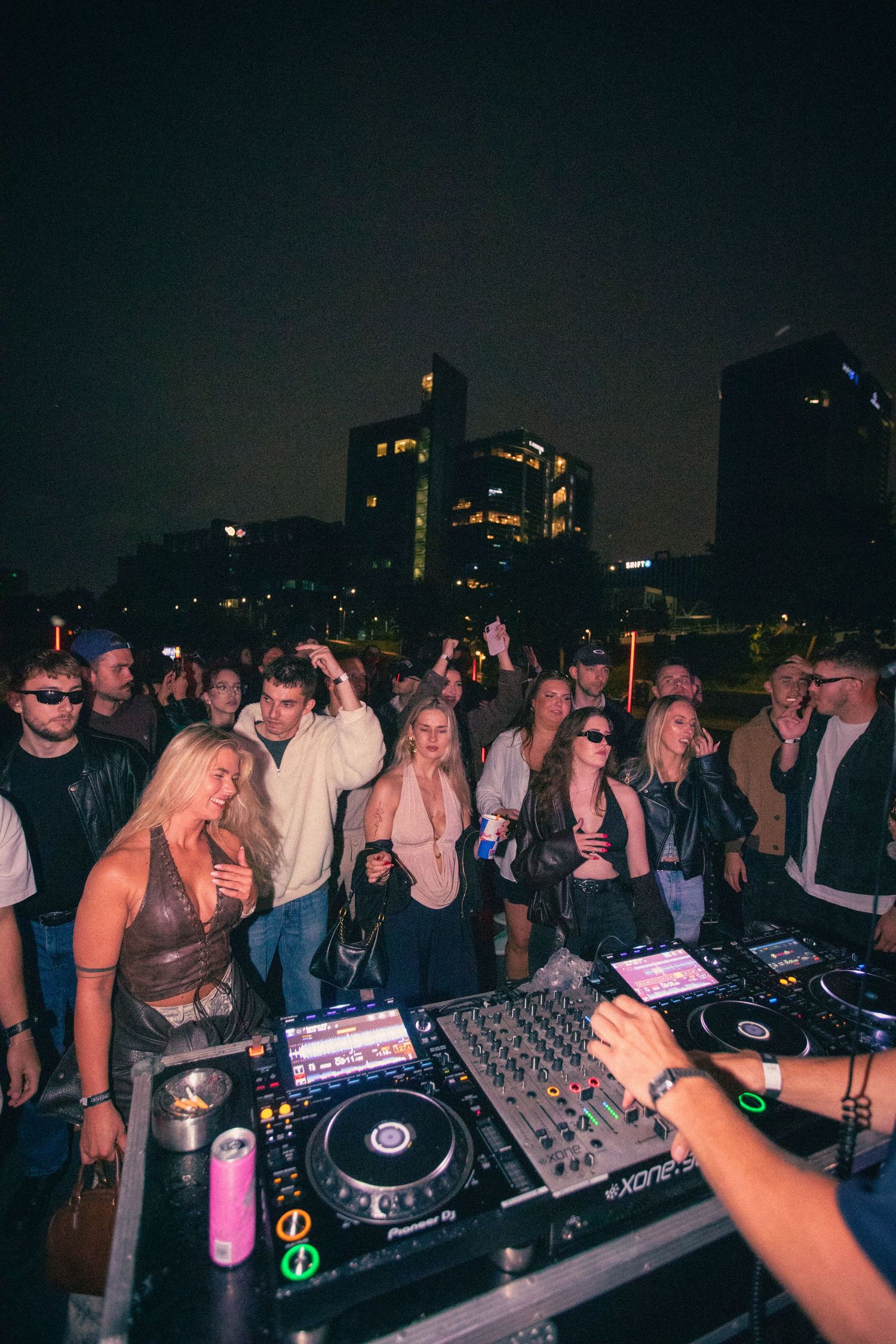DJ performing for an enthusiastic crowd at an outdoor rooftop nighttime music event.