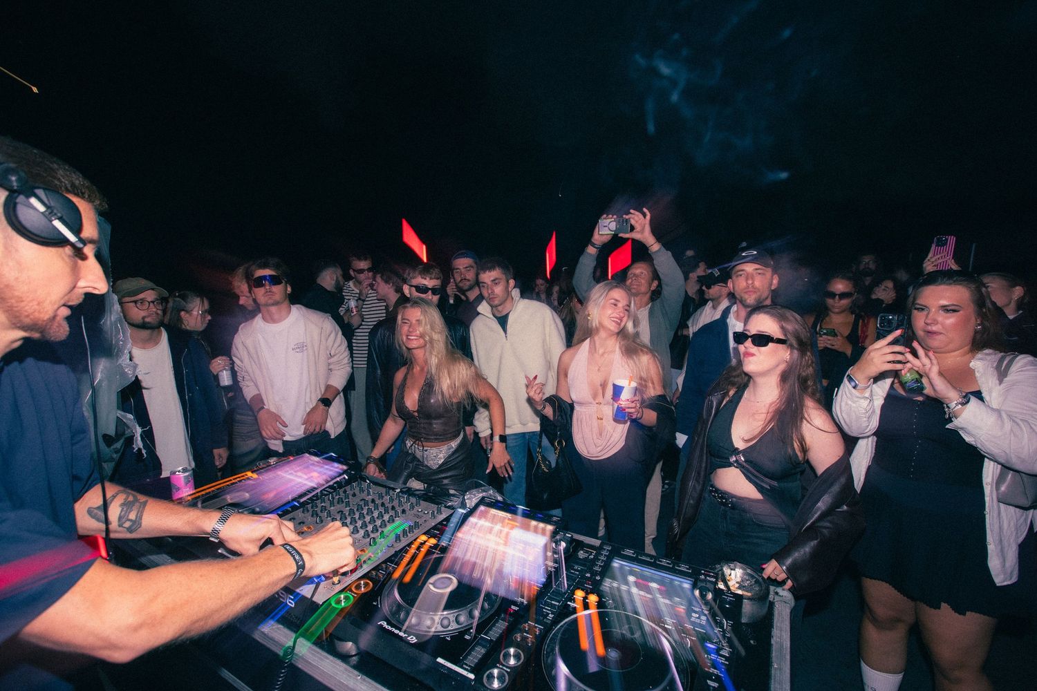 DJ performing for a large crowd at an outdoor nighttime festival with smoke effects.