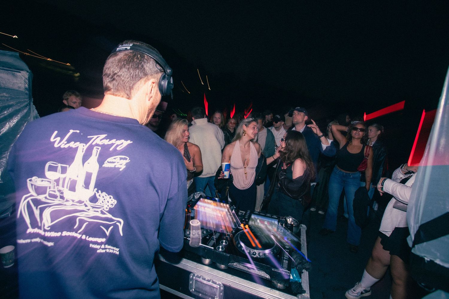 DJ wearing headphones and blue hoodie performing for a large crowd at an outdoor night event.