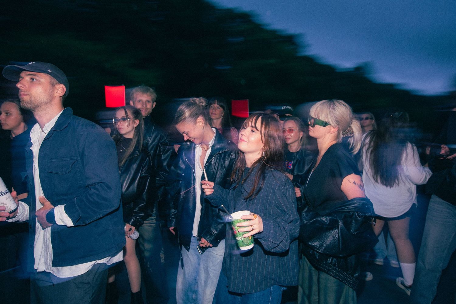 Crowd of young people enjoying an outdoor evening music festival event in casual and leather jackets.
