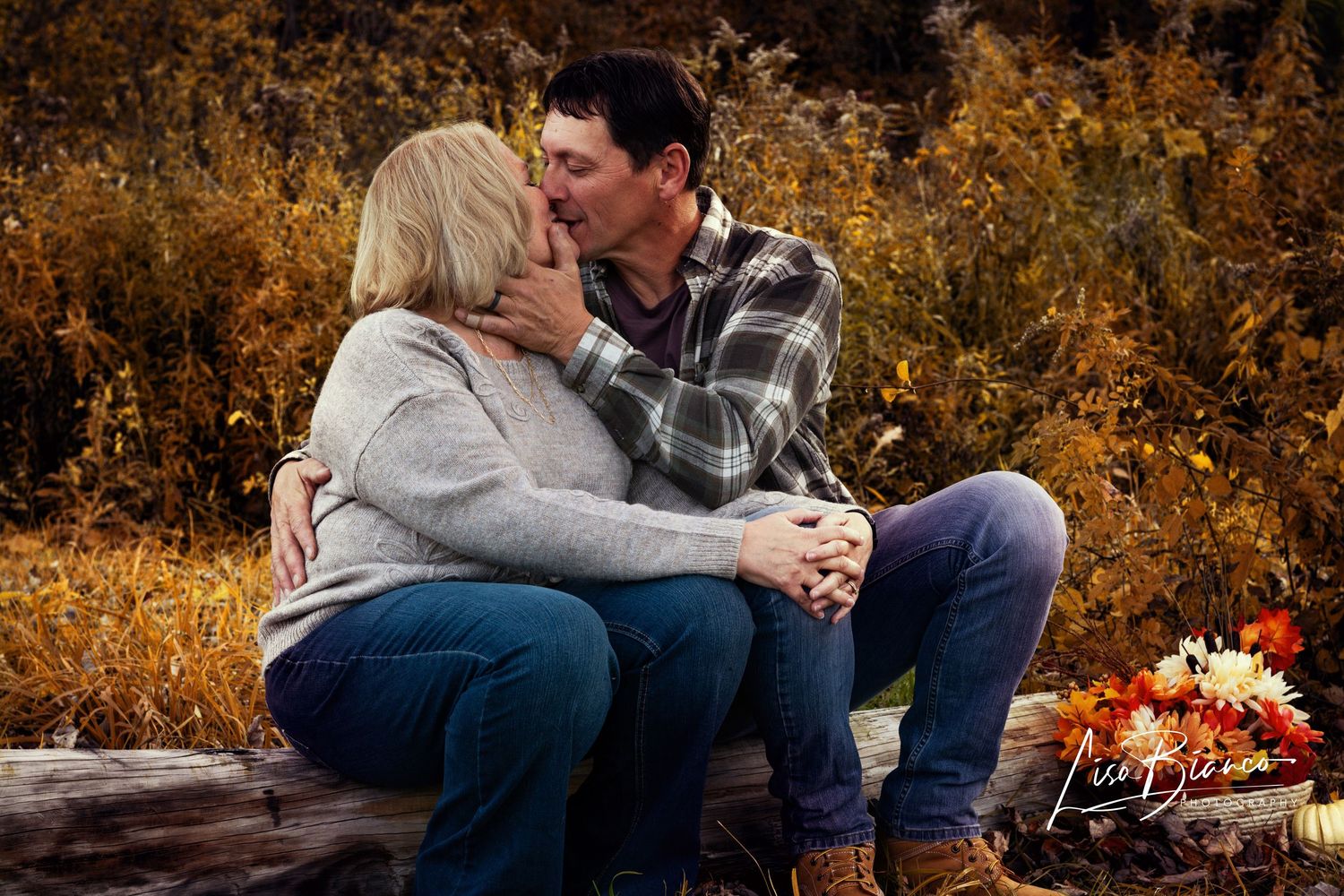 Couple sharing a romantic kiss outdoors during autumn, surrounded by golden foliage in a professional photo session.
