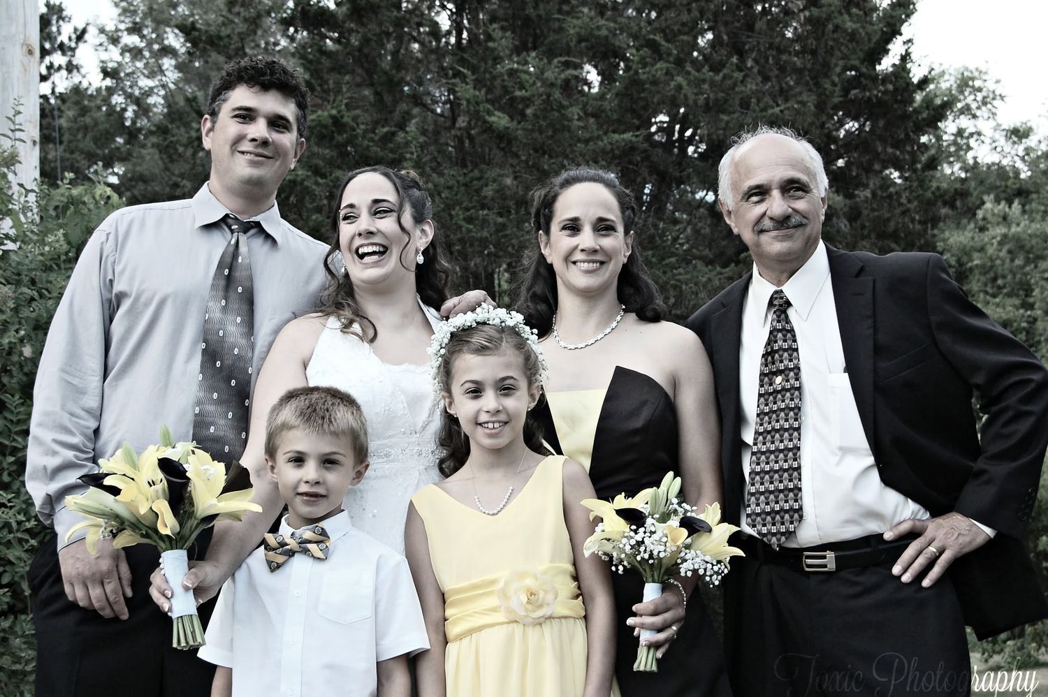 Family group photo at a wedding with bride, groom, and relatives including children in formal attire outdoors.