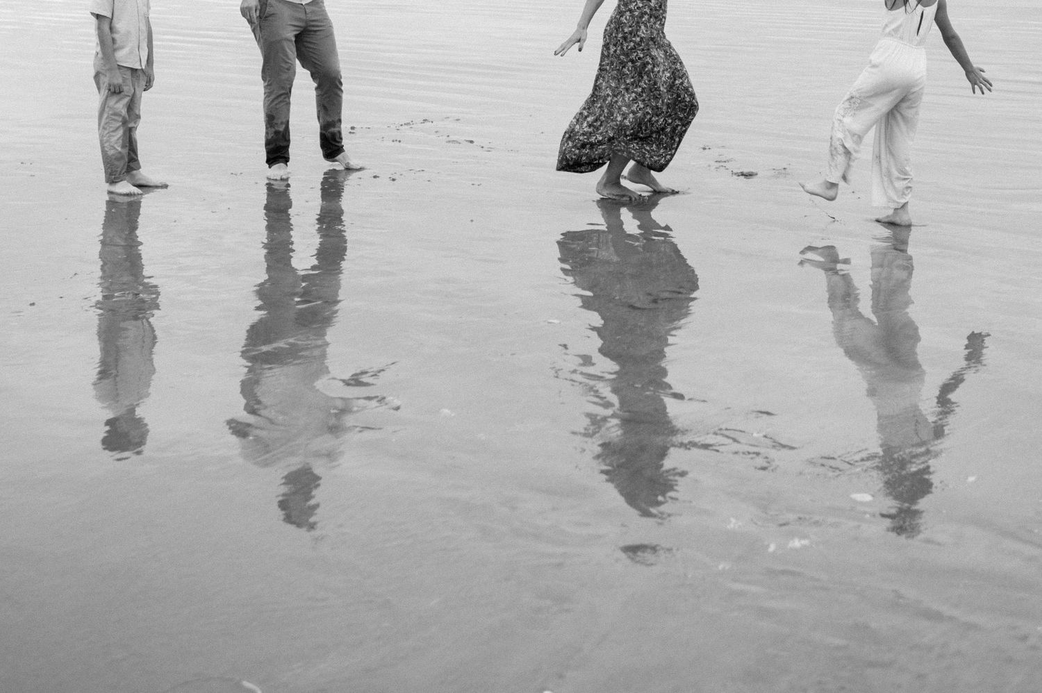 Black and white photo of a family walking on a reflective wet beach, their figures mirrored in the water.