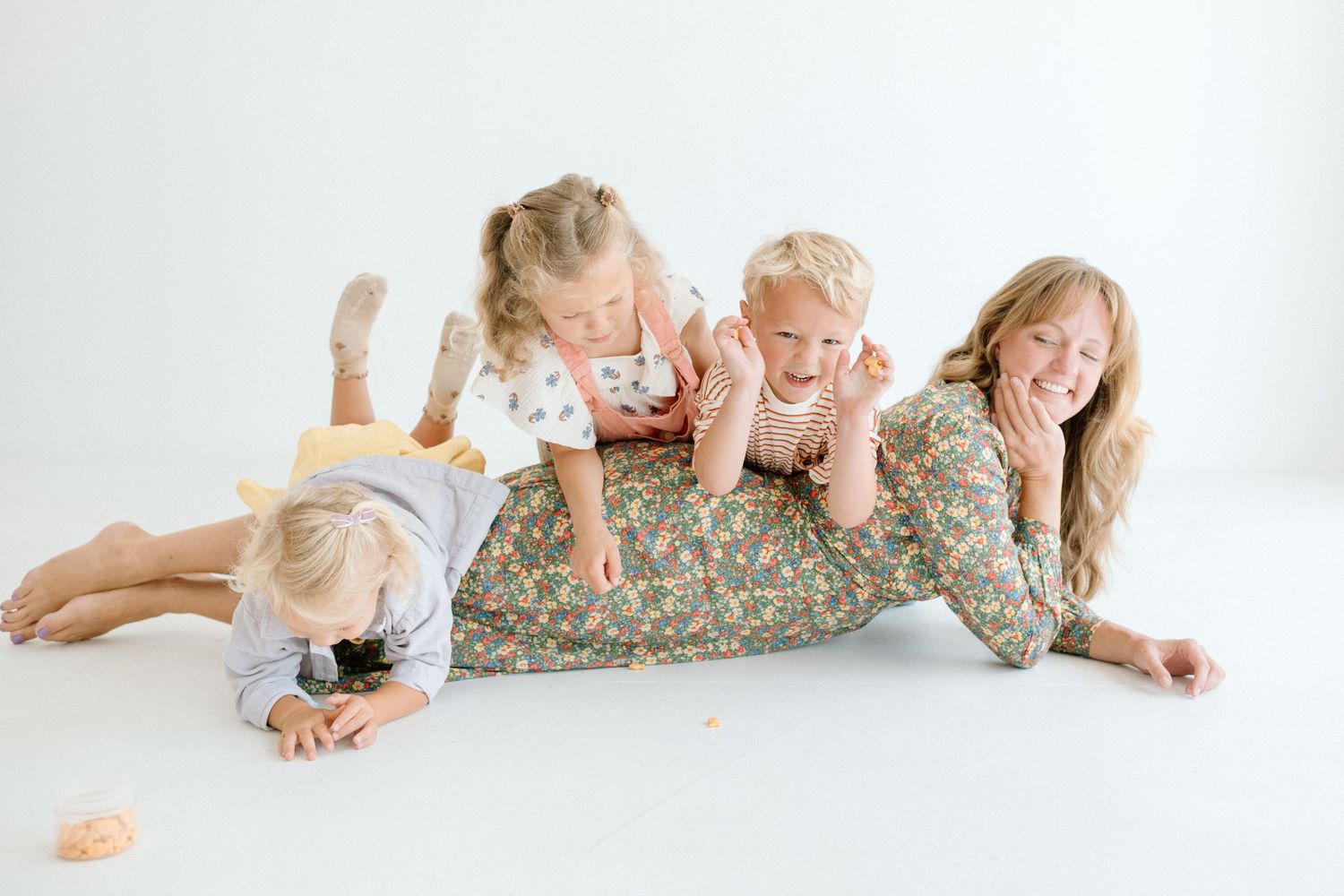 Four playful children laughing and tumbling together on white studio floor.
