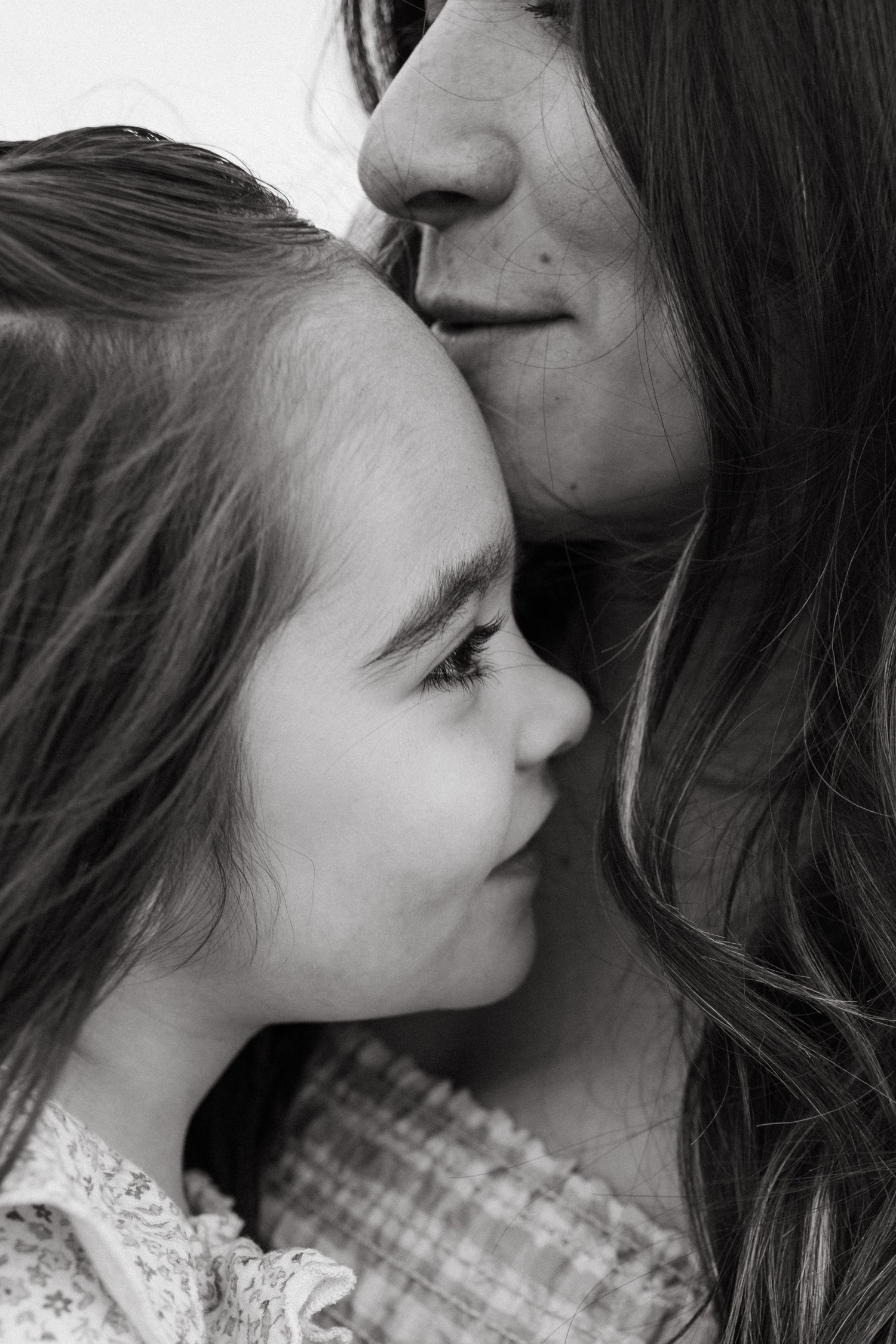 Black and white close-up of a mother gently kissing her young daughter on the forehead.
