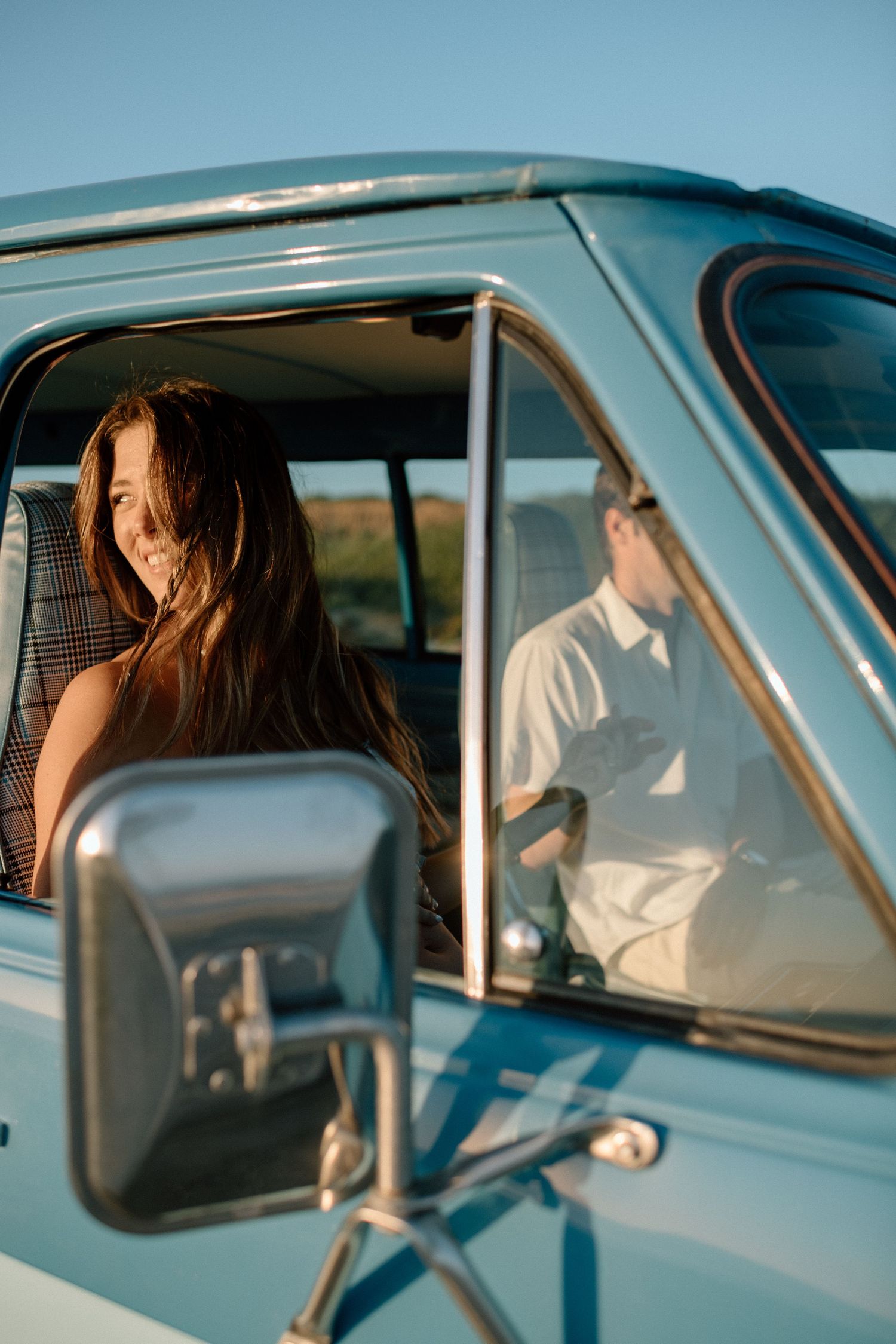 Two people sit inside a vintage blue vehicle during golden hour.