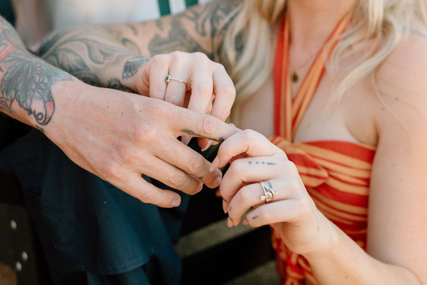 Close-up photo of tattooed hands exchanging rings during a wedding ceremony.