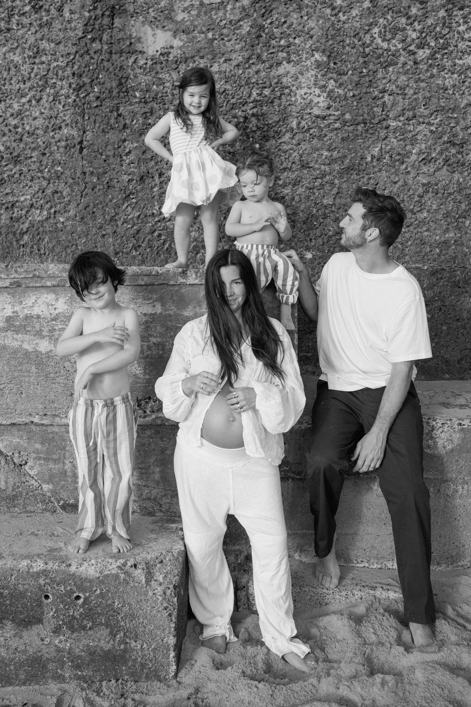 Black and white family portrait of pregnant mother, father, and three children on stone steps.