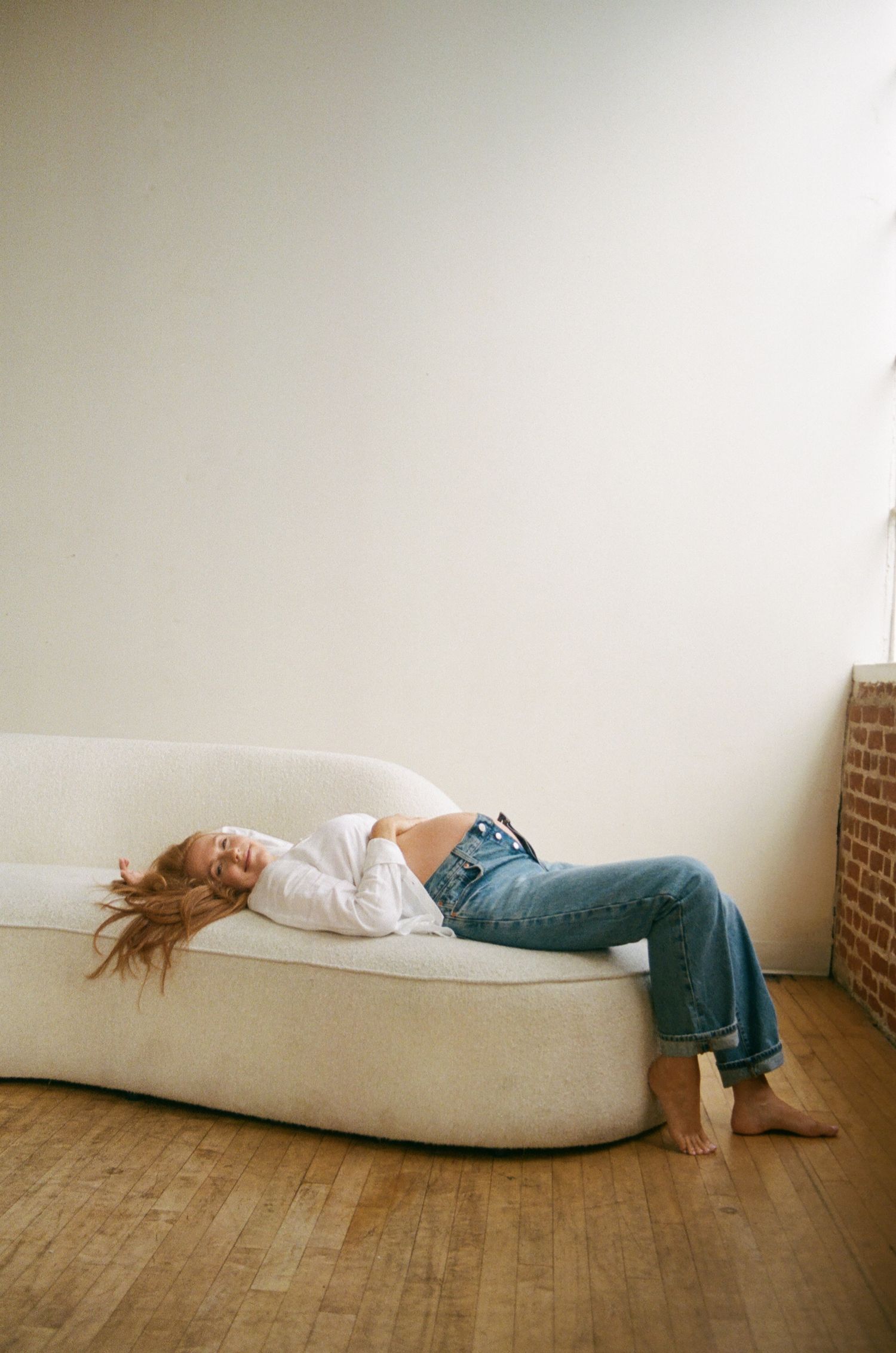 Pregnant woman in white shirt and jeans relaxing on a curved cream sofa.