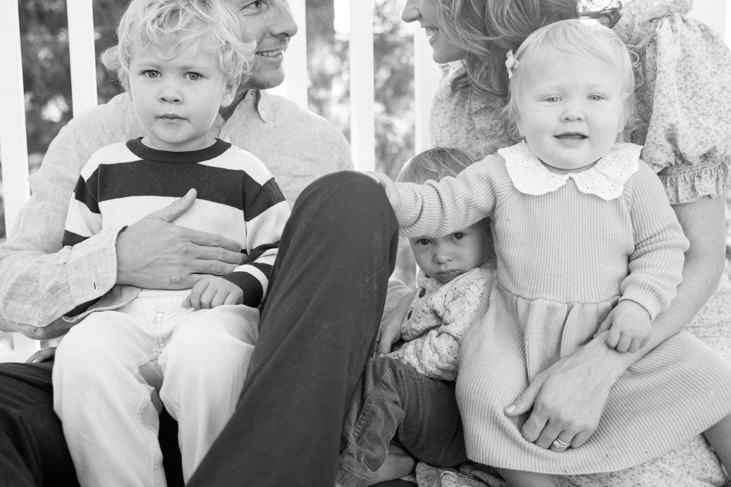 Black and white vintage photo of grandparent sitting with three young children outdoors.