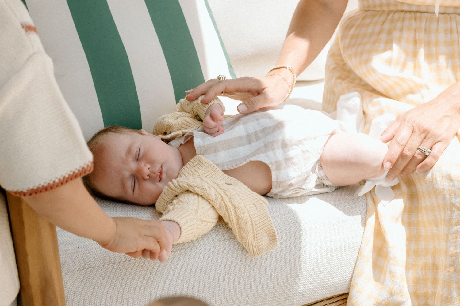 A peaceful newborn baby sleeping on a chair, gently held by two adults in soft natural light.