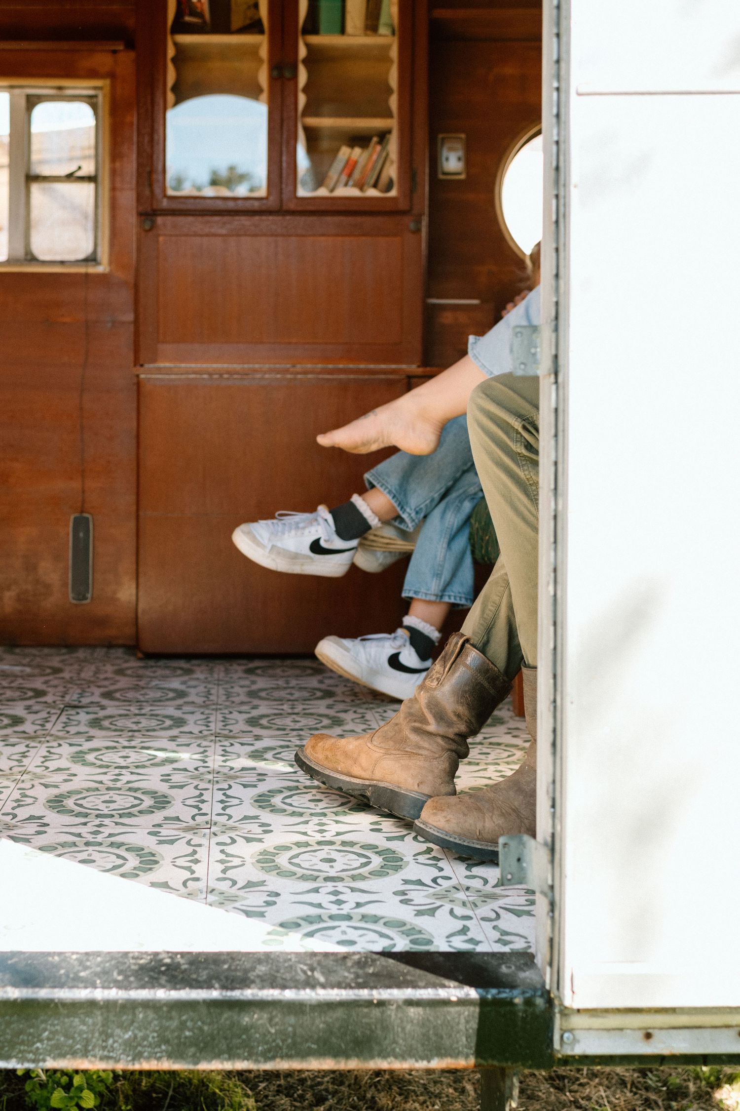 Two people sitting in a vintage camper doorway, one wearing Nike sneakers and the other brown leather boots.