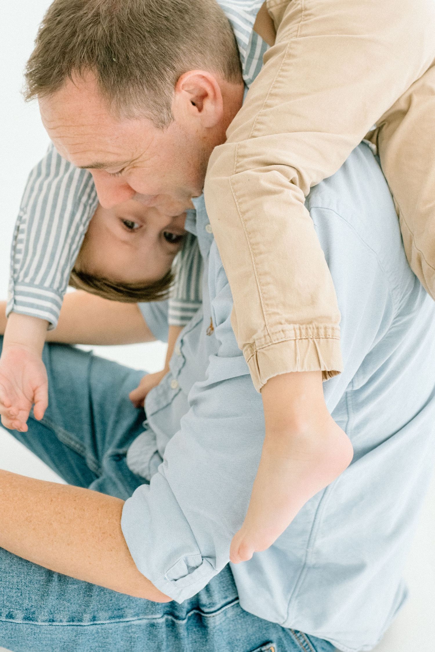 Father playfully holding young child upside down, both laughing during fun family photo session.