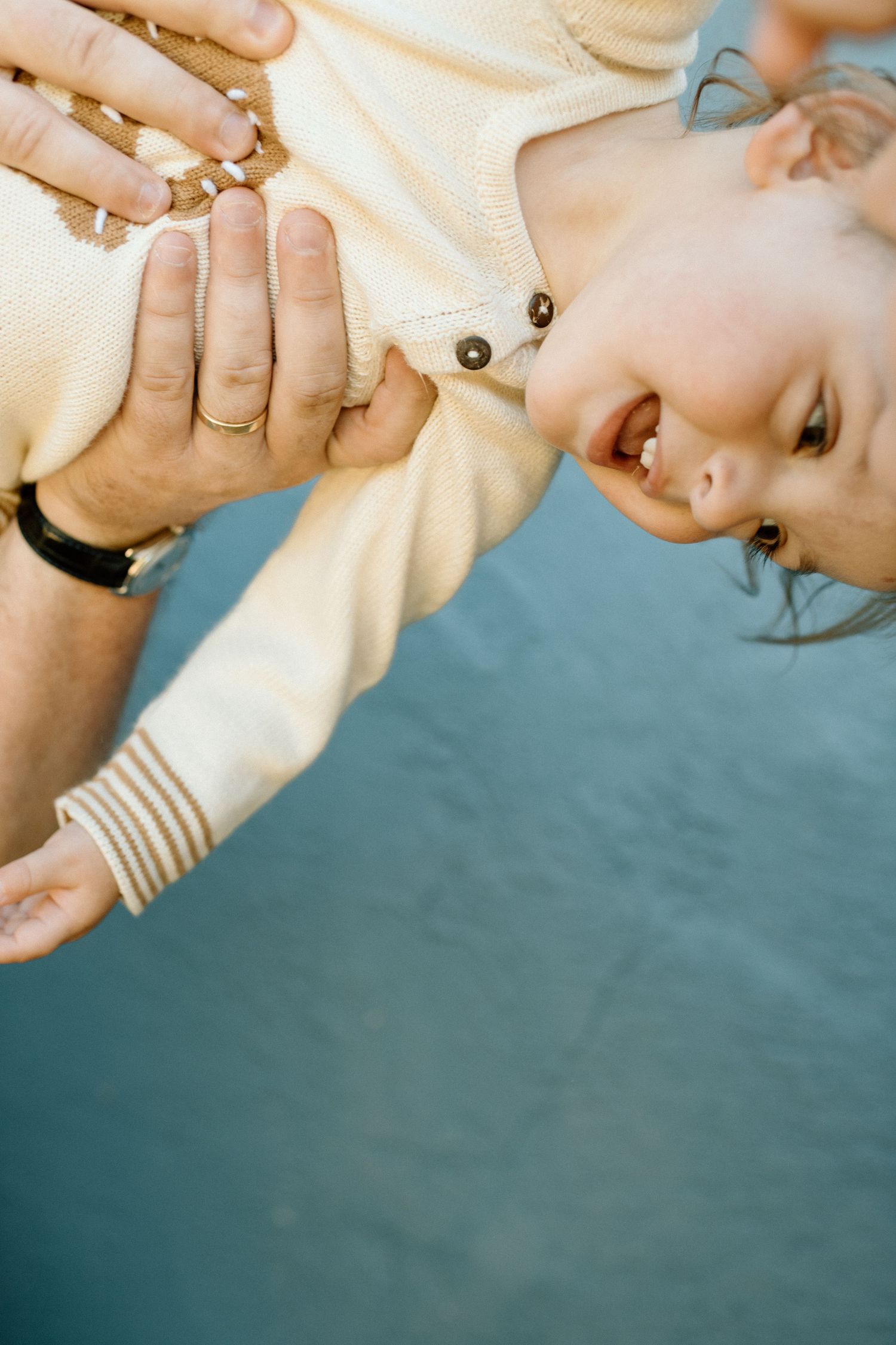 A parent holds a laughing baby upside down over a blue water background.
