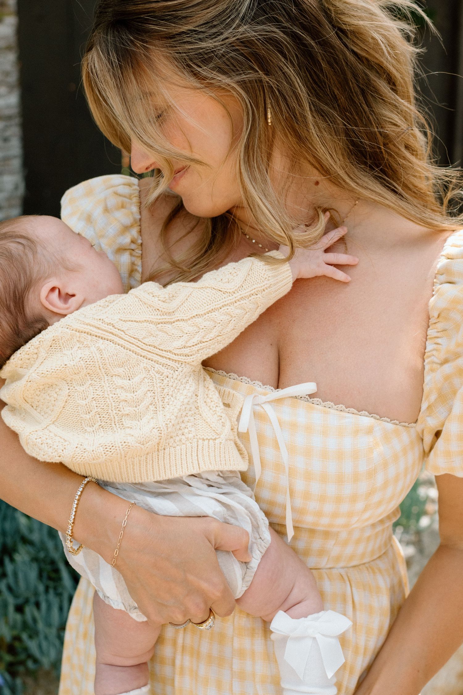 A mother in a yellow gingham dress tenderly holds her newborn baby close while gazing down lovingly.