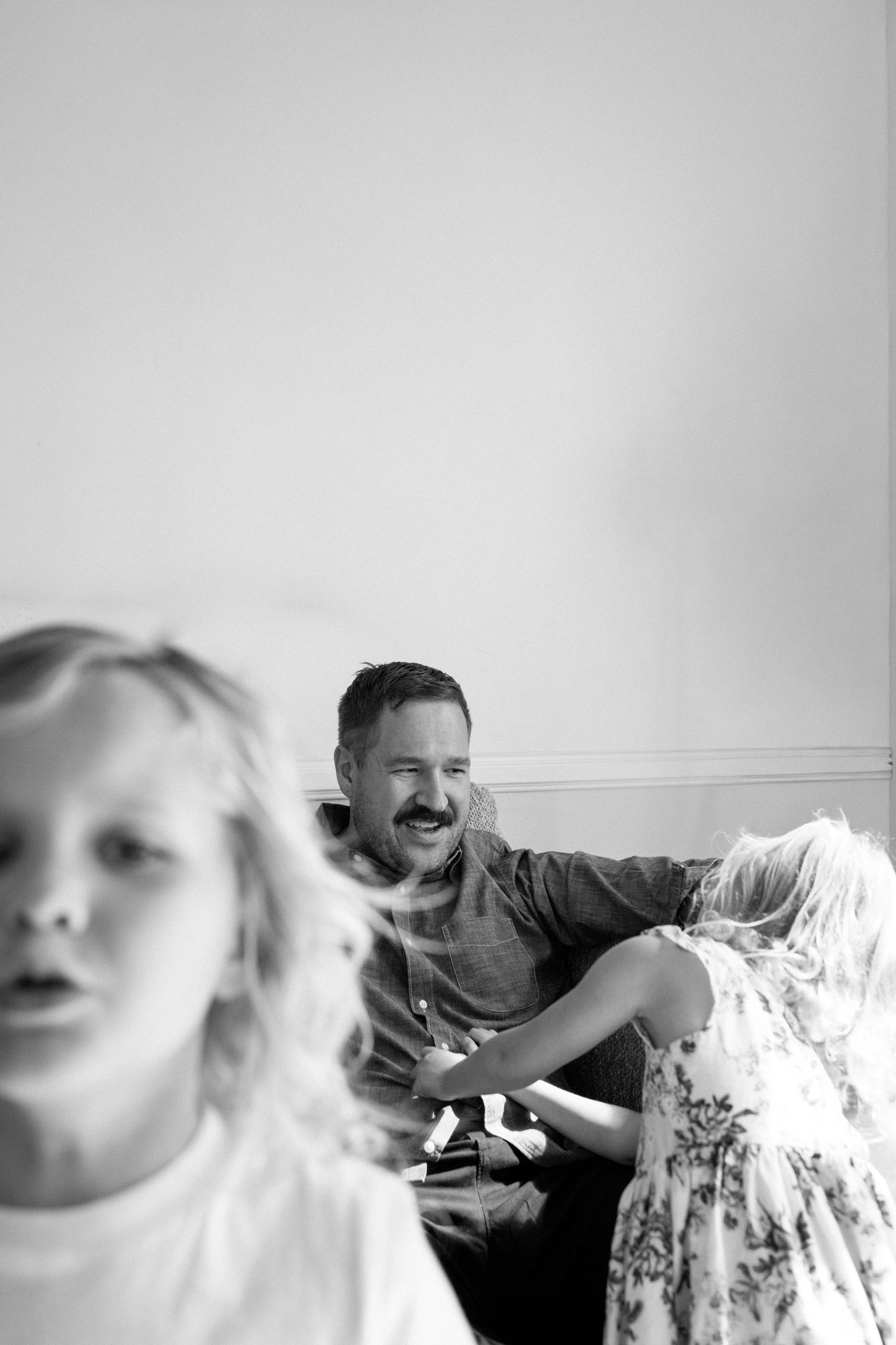 Black and white photo of a smiling father playing with his two young children indoors.