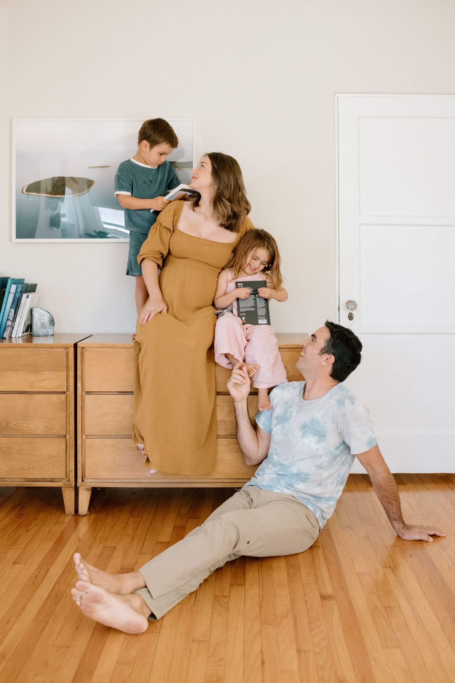 A happy family of four relaxes together in a bright modern living room with wood floors.
