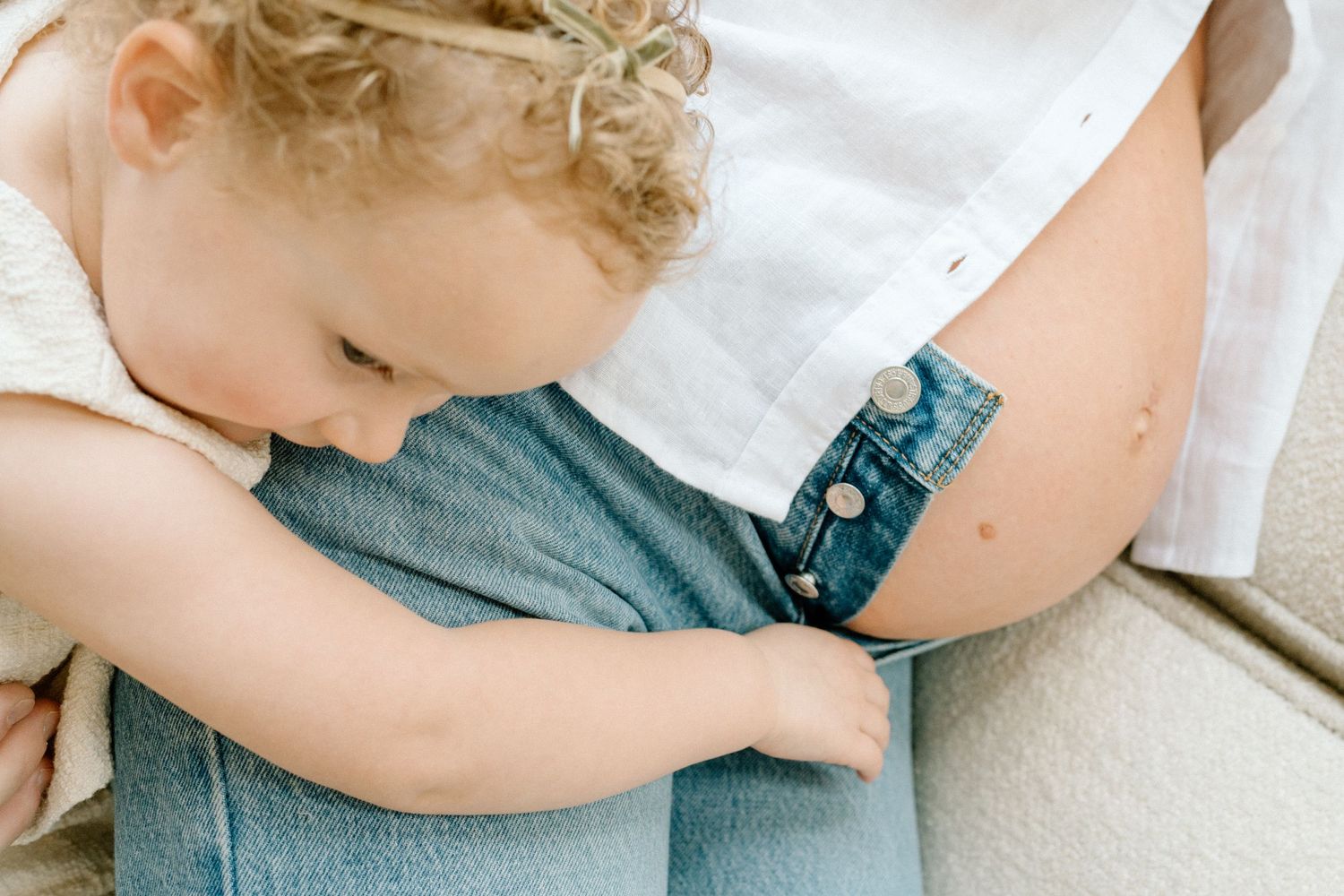 Curly-haired toddler gently hugging pregnant mothers belly in a sweet embrace.