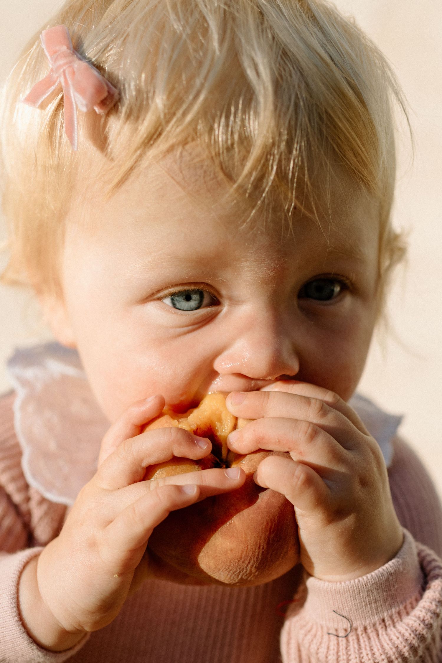 Adorable blonde toddler girl with blue eyes eating a bread roll with both hands.