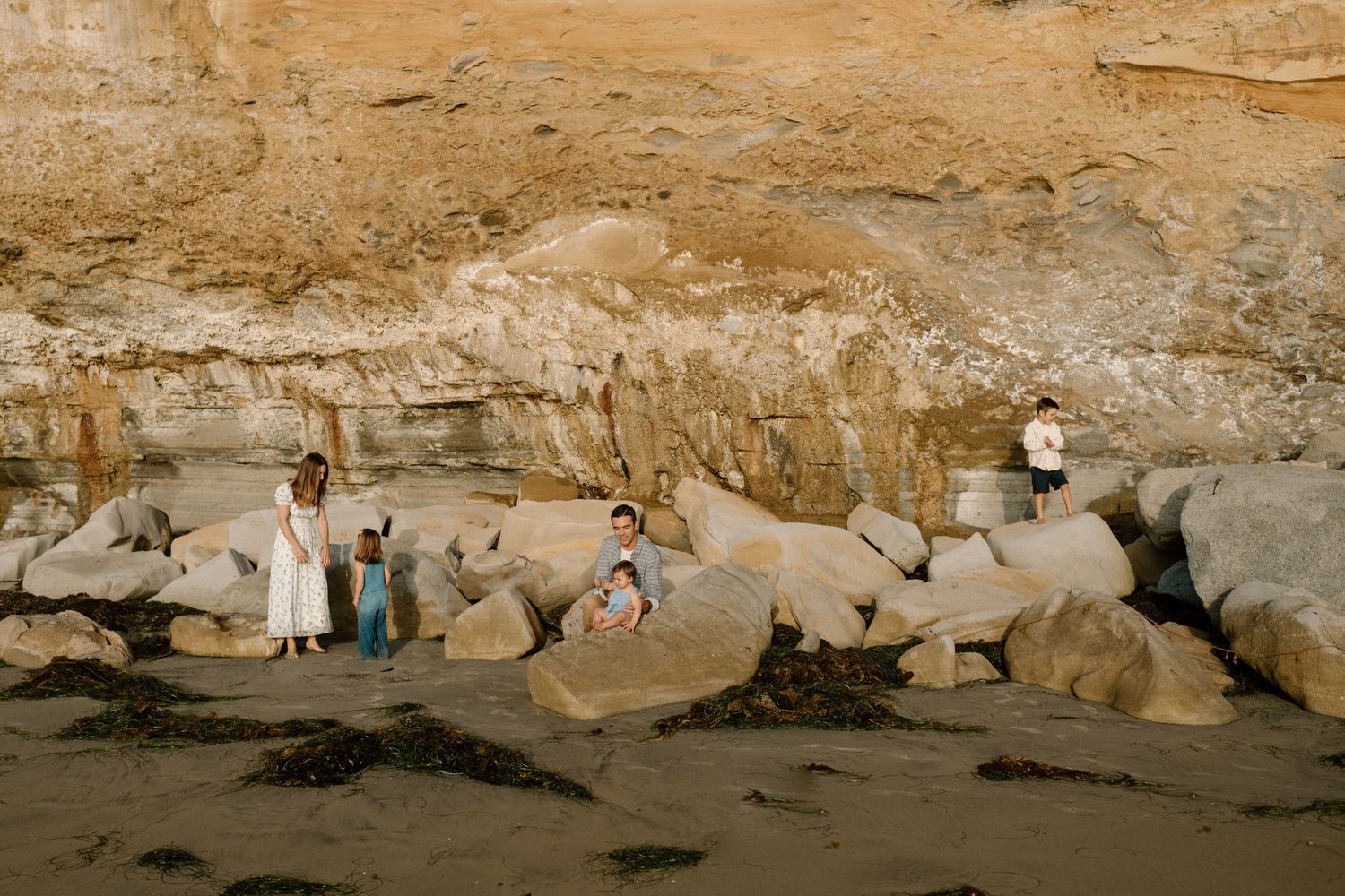 Family explores rocky beach area at base of tall sandy coastal cliffs.