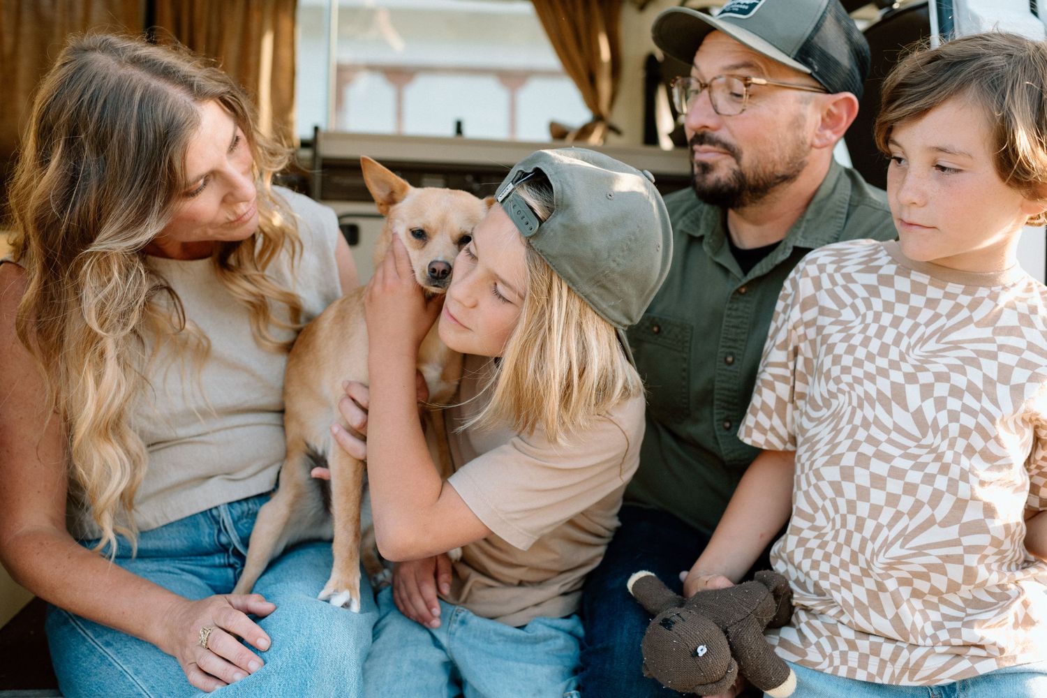 Family with two kids and a small dog sharing a tender moment near a vintage camper.