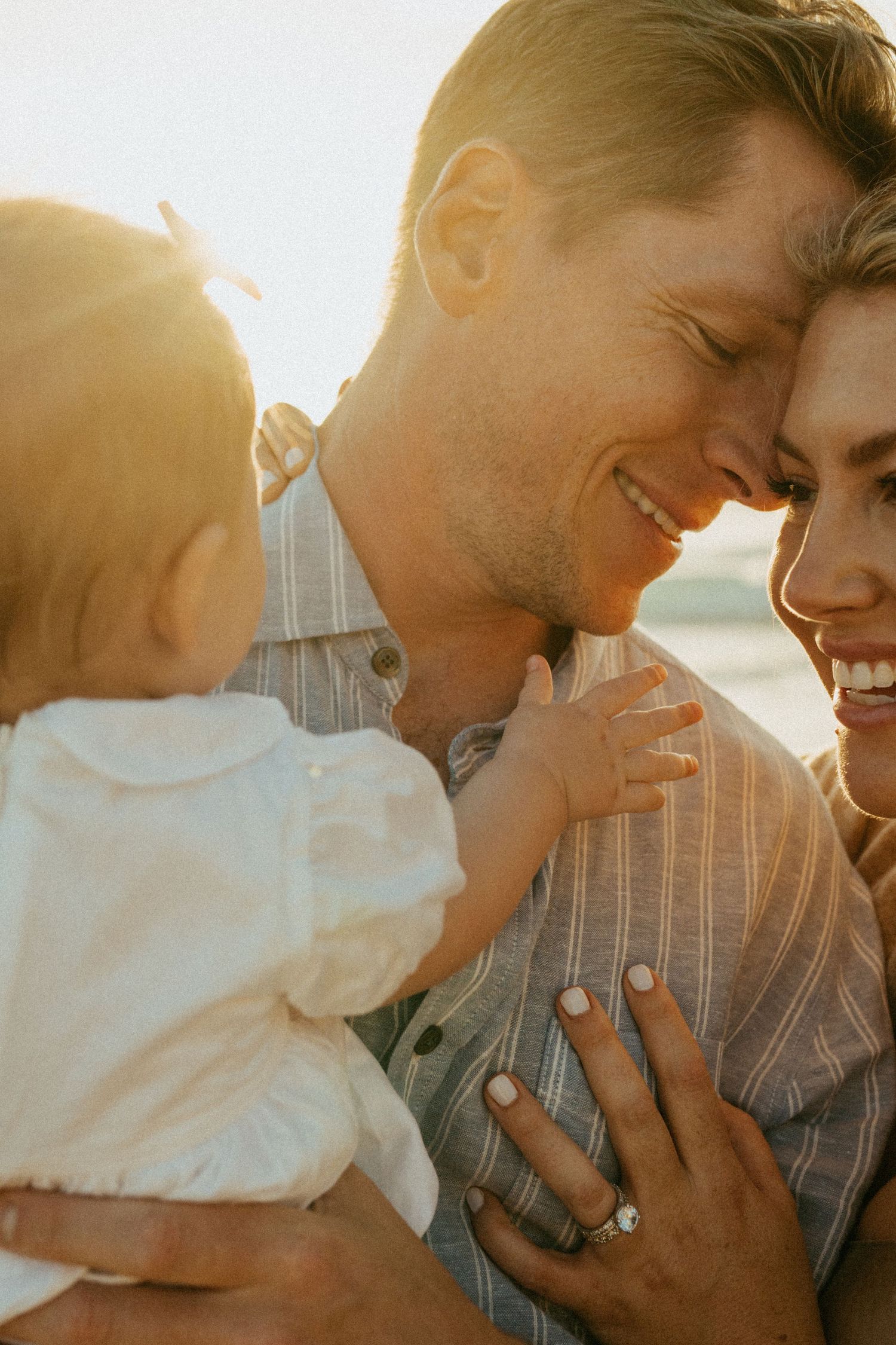 Happy couple smiling together while holding their baby outdoors in warm golden sunset light.