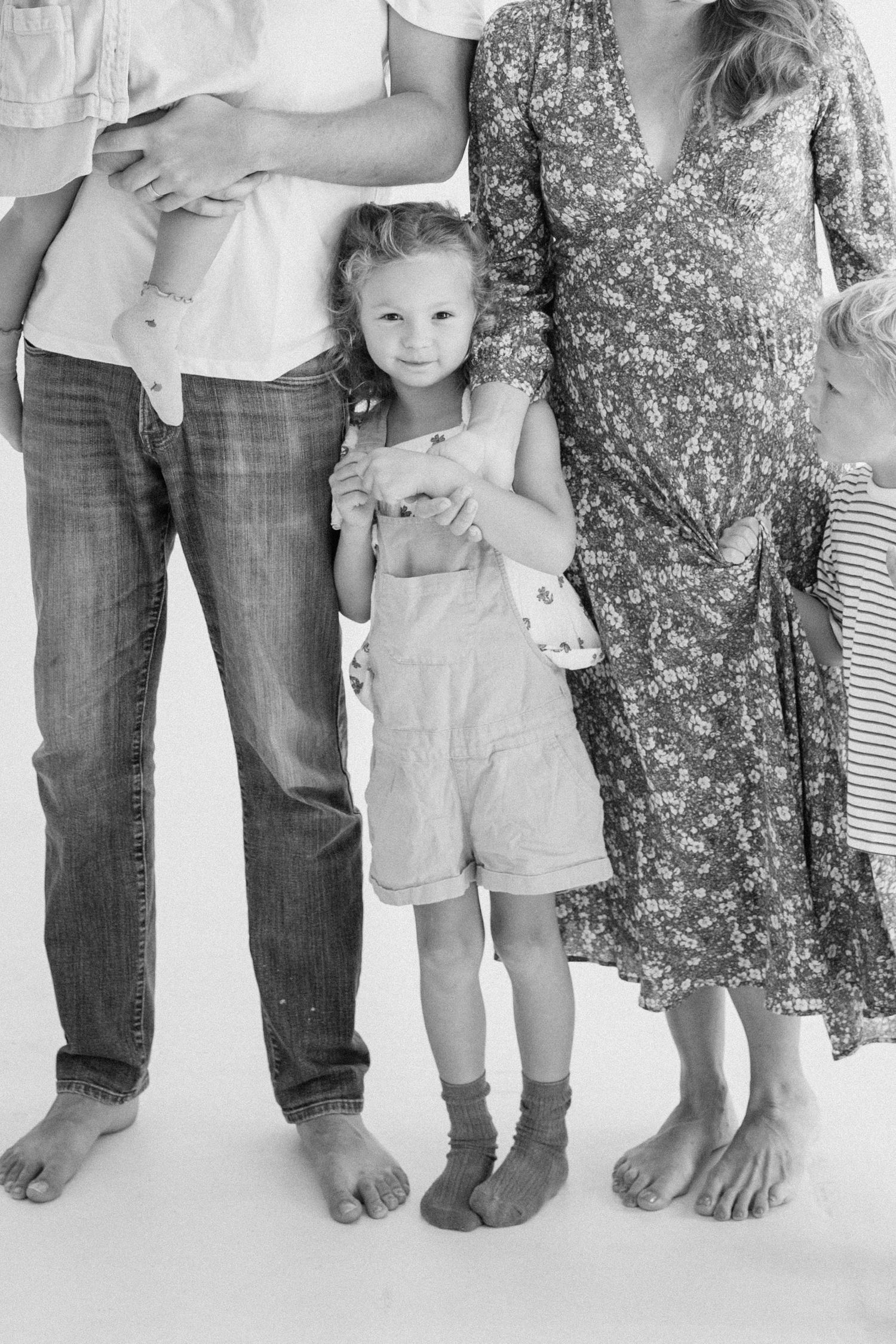 Black and white photo of a young girl in overalls standing between her parents and sibling.