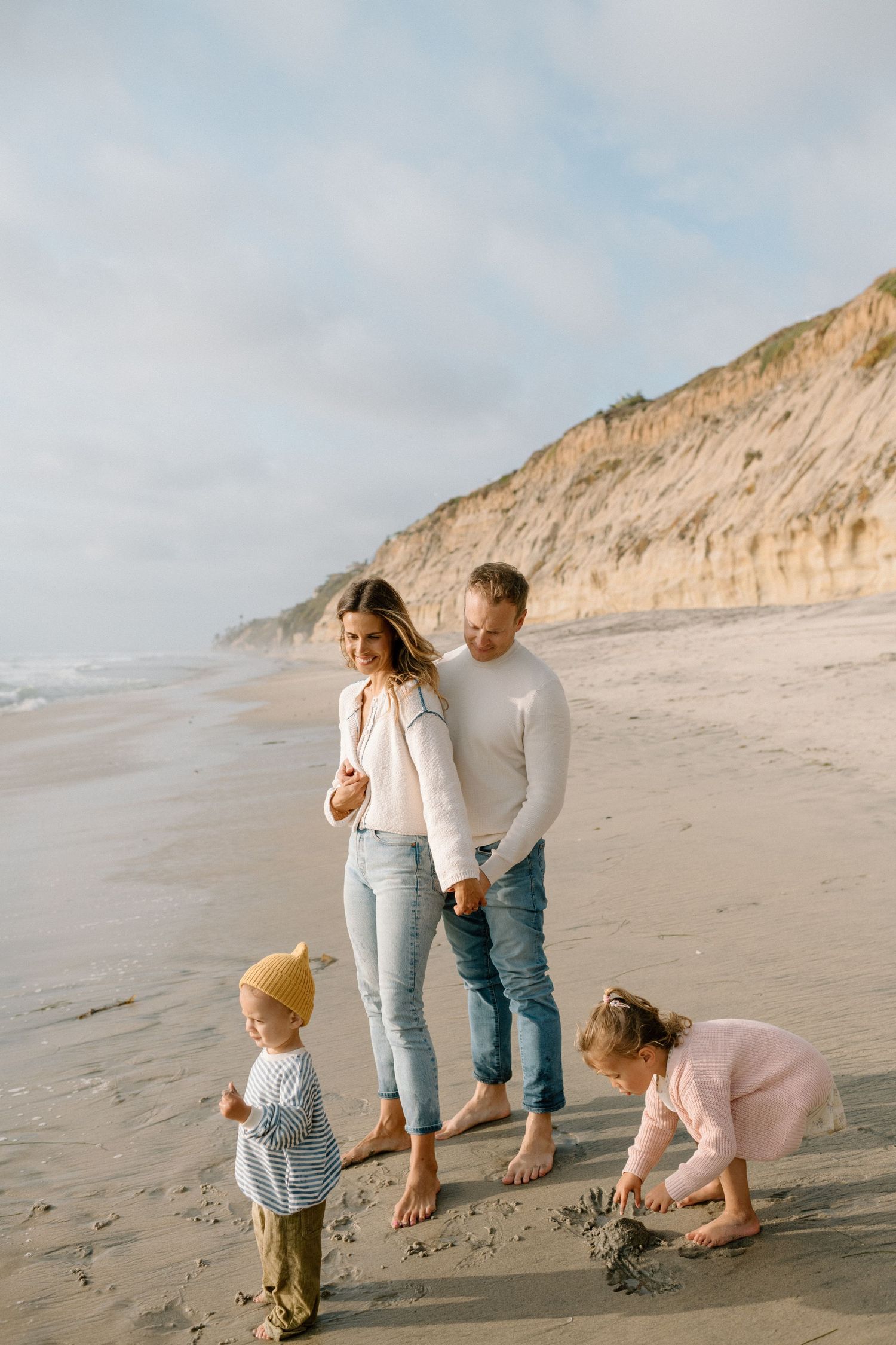 Family with two young children playing on a sandy beach with cliffs in the background.