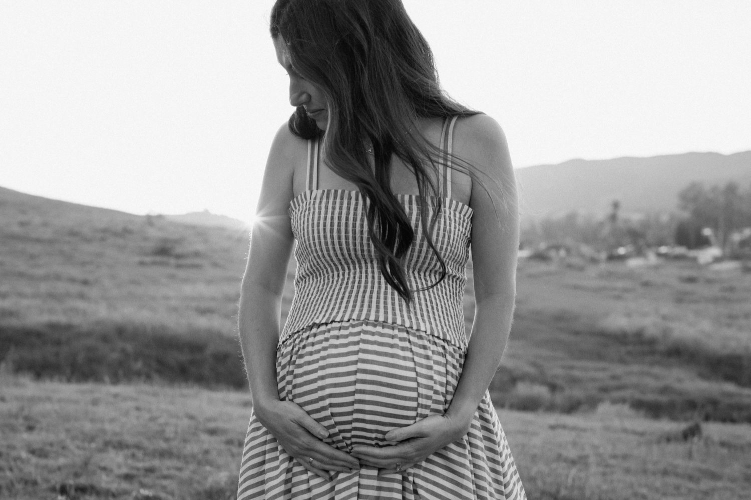 Black and white photo of pregnant woman in striped dress holding belly.