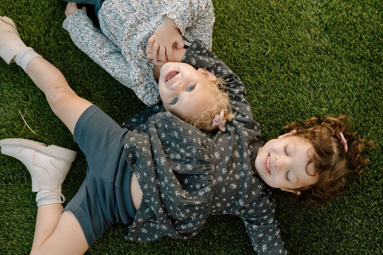 Two young children laughing and lying on green grass together.
