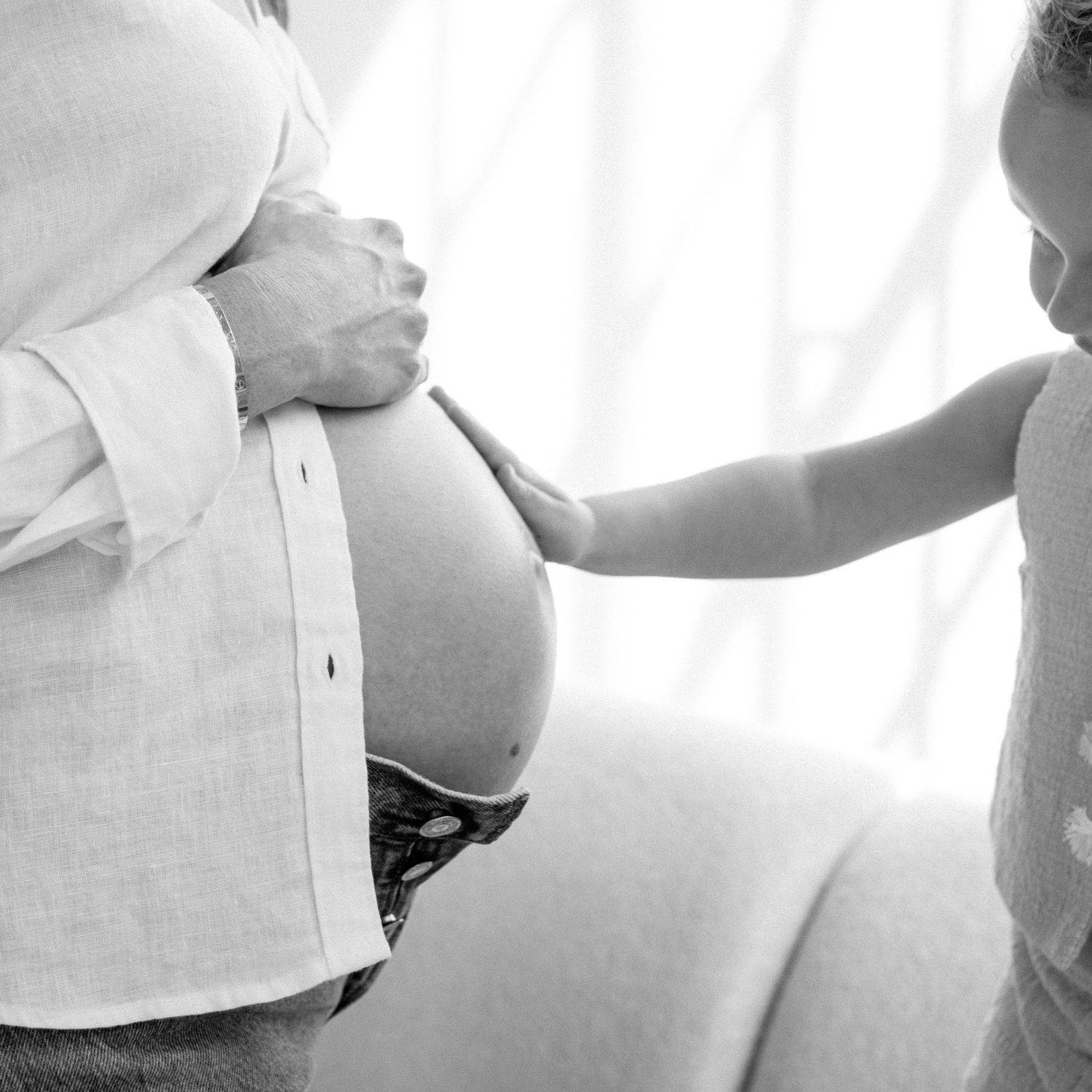 Black and white photo of a child touching a pregnant mothers bare belly.
