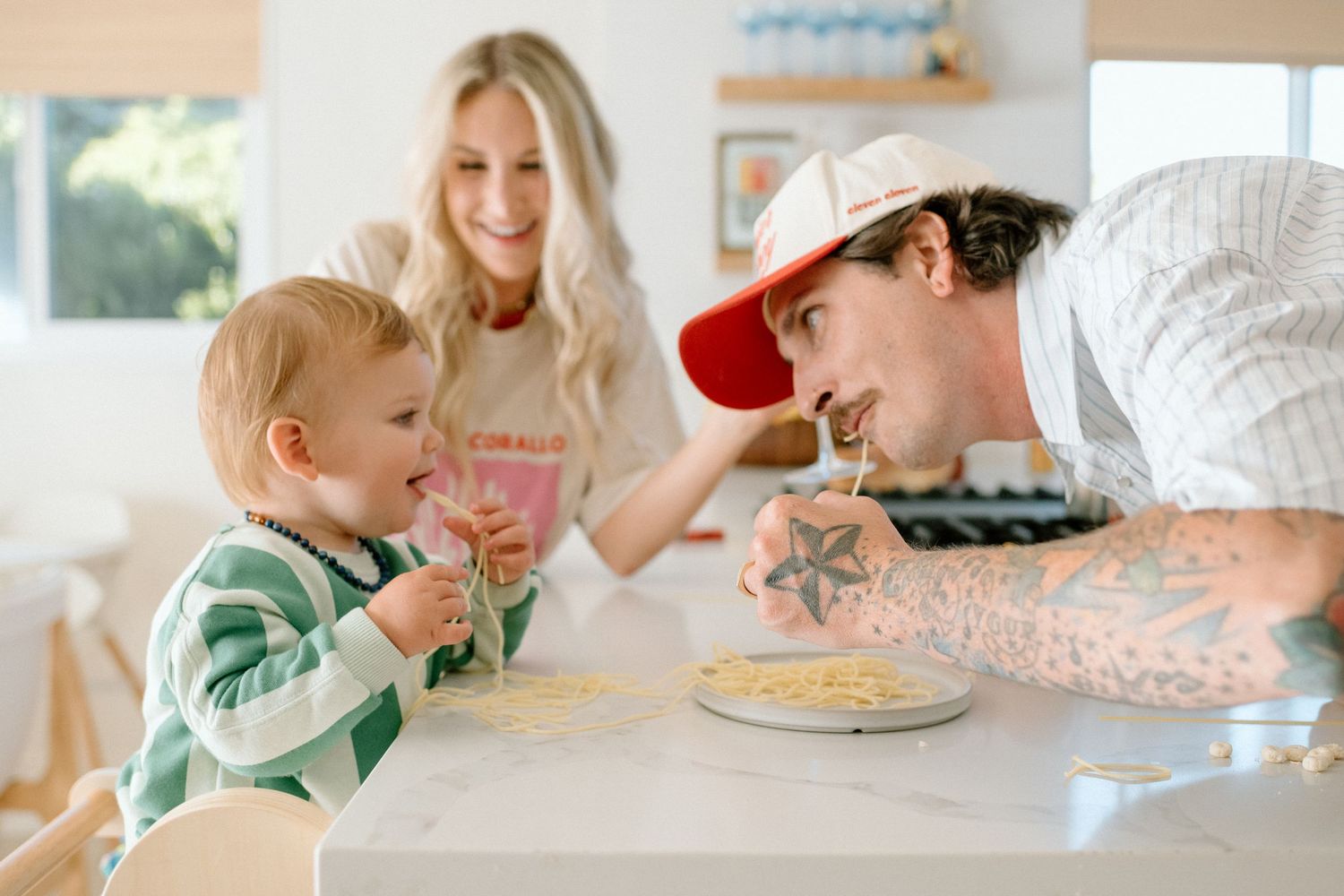 A family enjoys breakfast together at the kitchen counter while smiling and laughing with their pet cat.