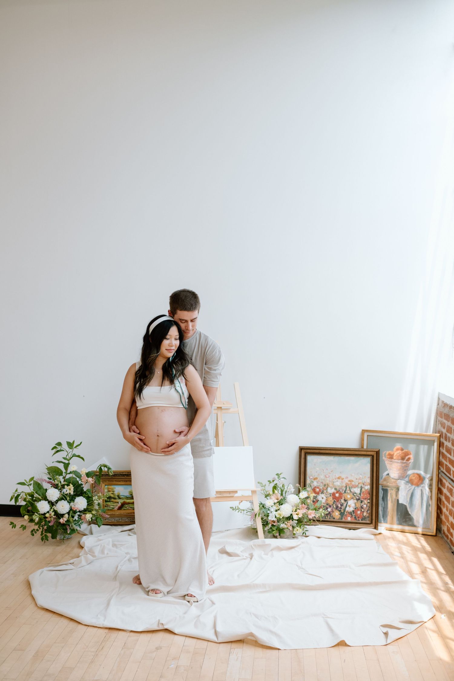 Standing man embraces pregnant wife during maternity photoshoot in a San Diego studio.