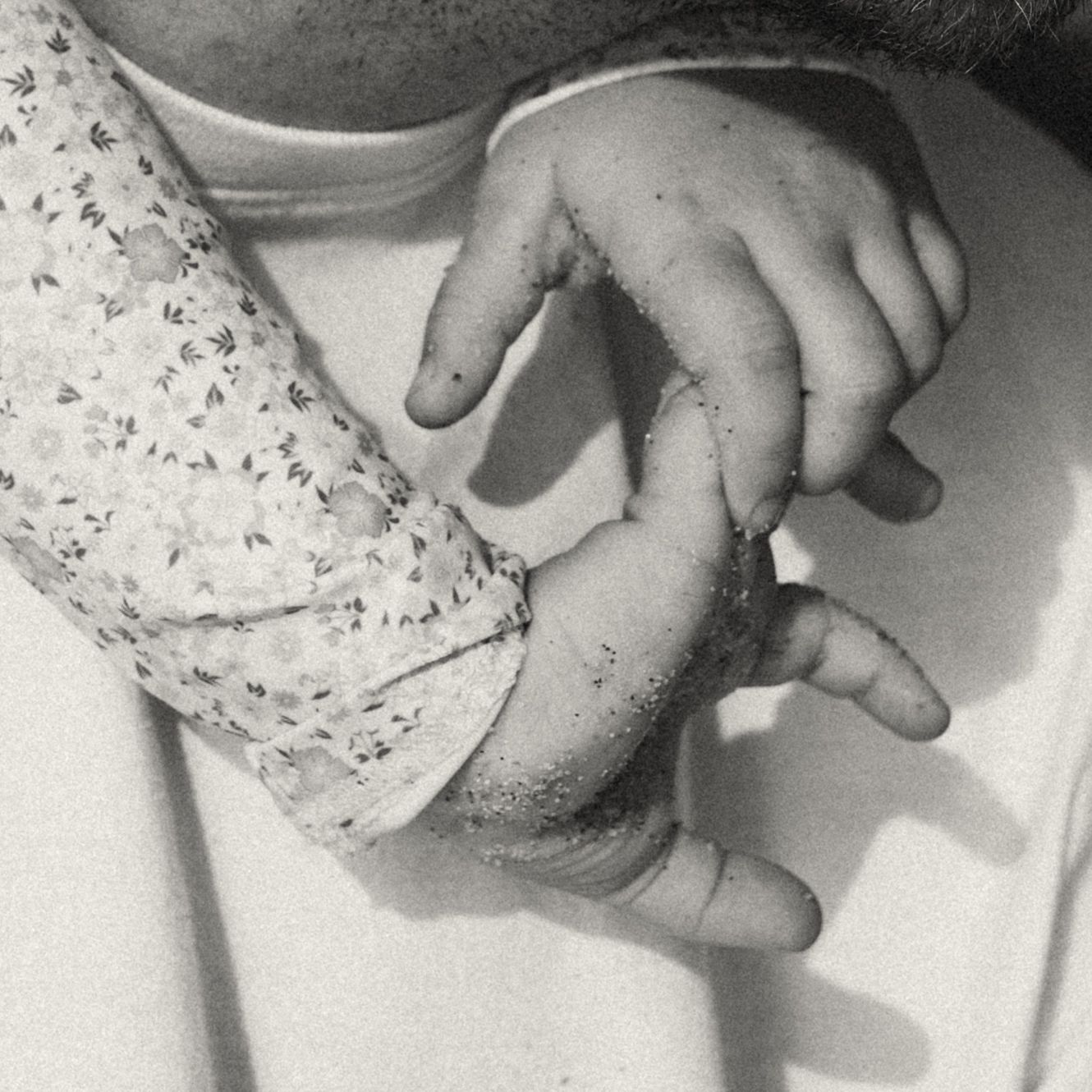 Black and white photo of a baby's small hand gently grasping an adult's larger hand.