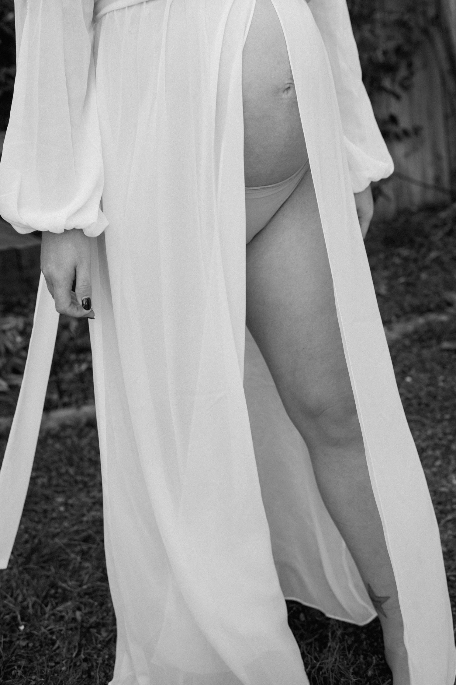 Black and white photo of a pregnant woman in a flowing white robe outdoors.