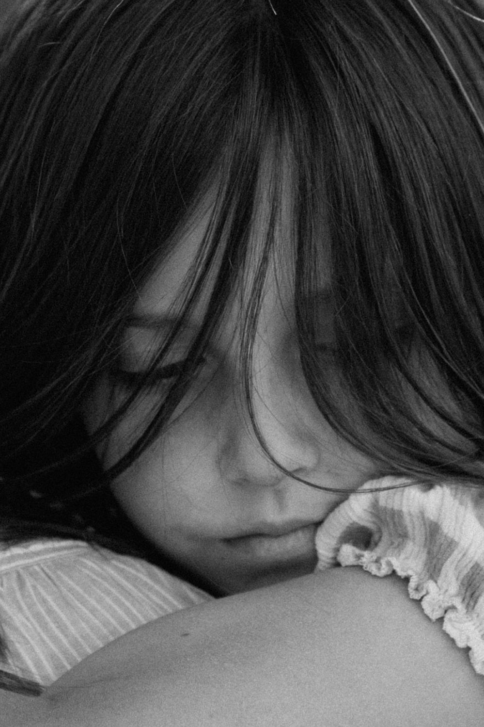 Black and white close-up of young girl with dark hair resting her head on a shoulder.