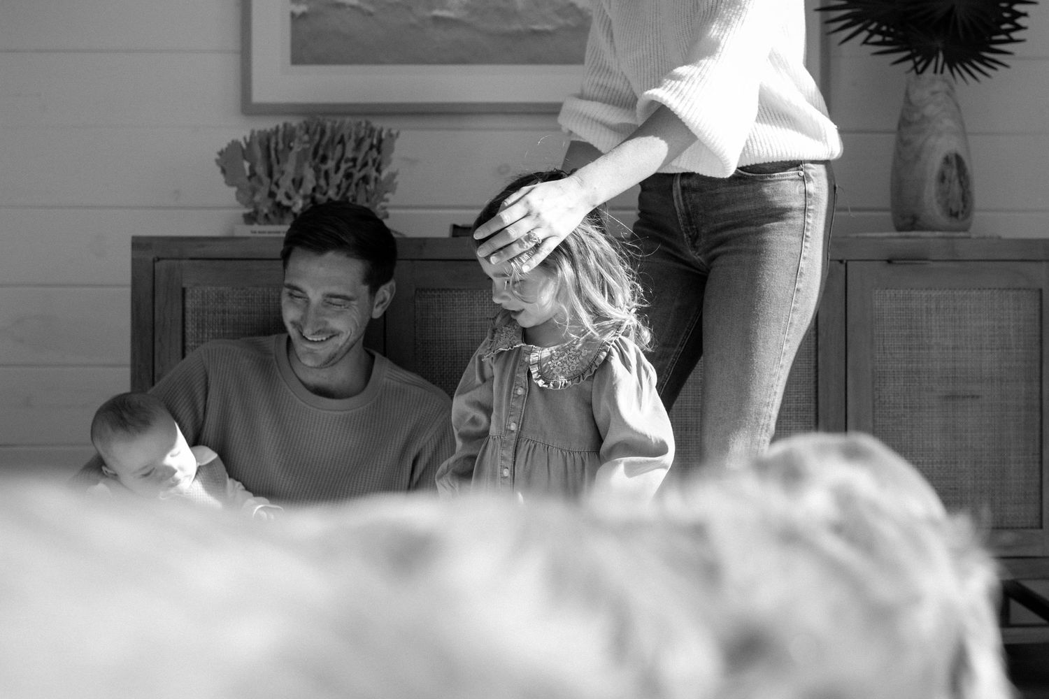 Black and white candid family photo of laughing dad with kids and mother ruffling hair.