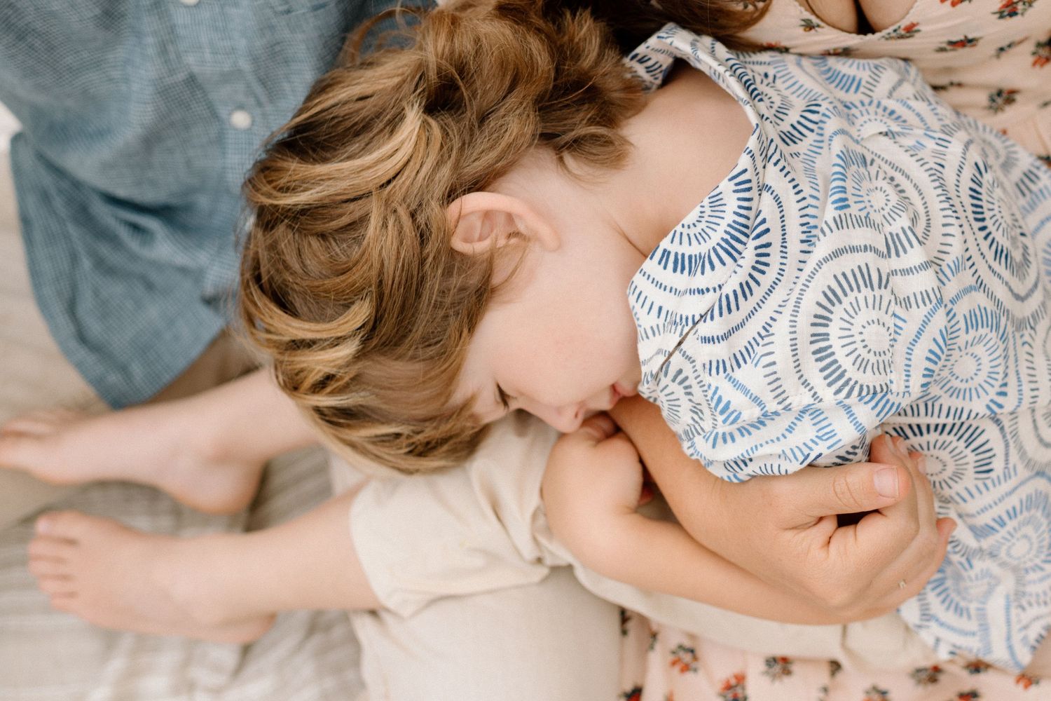 Overhead view of a curly-haired toddler snuggling into a parent's lap on a blanket.