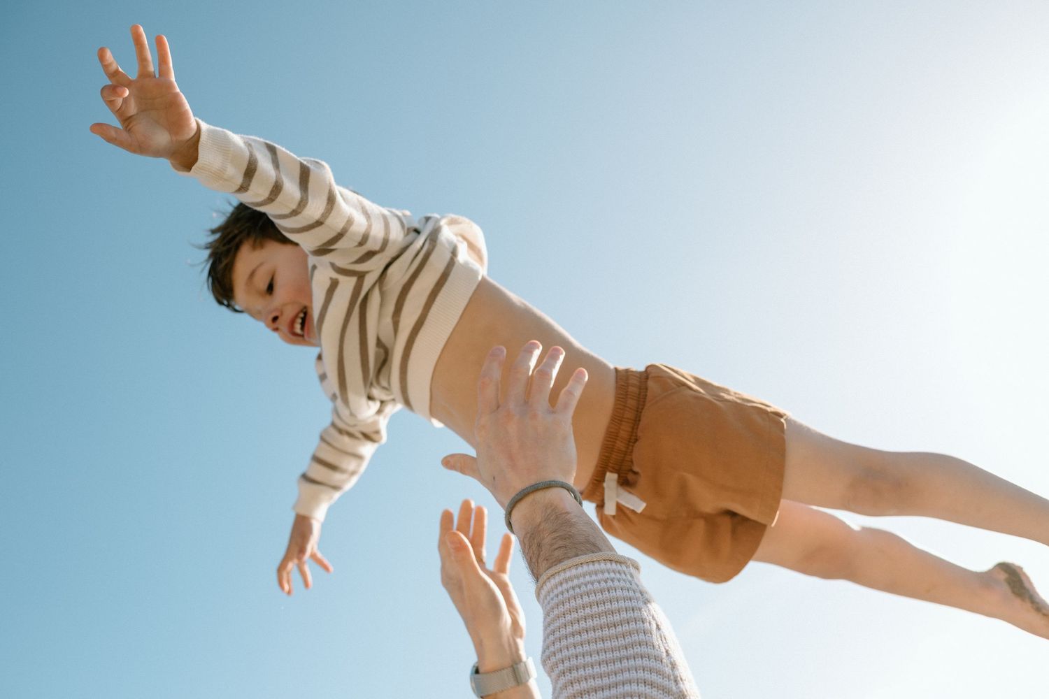 Father tossing laughing child into the air against a clear blue sky.