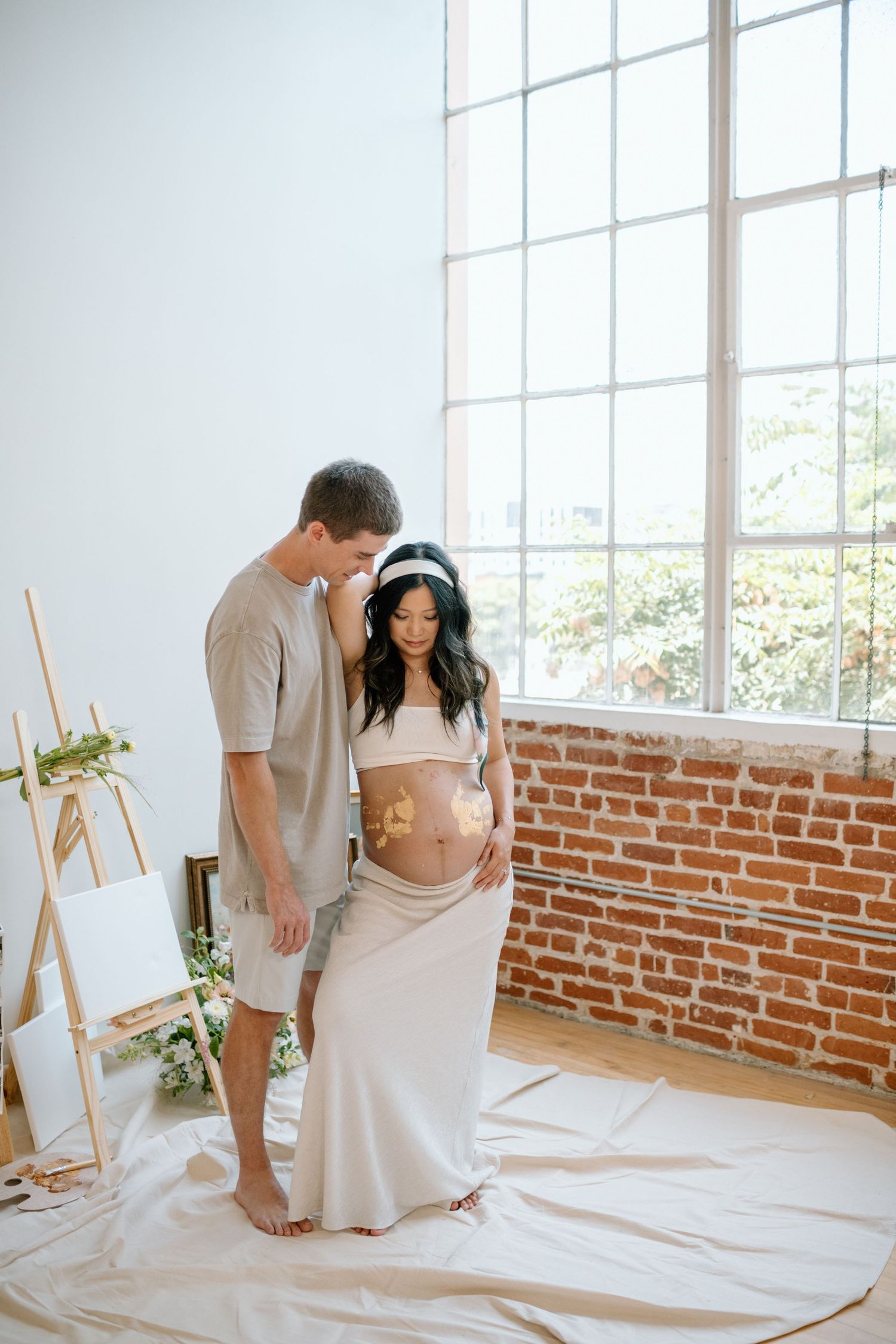 Man embraces pregnant wife's painted belly during maternity photoshoot in a San Diego studio.