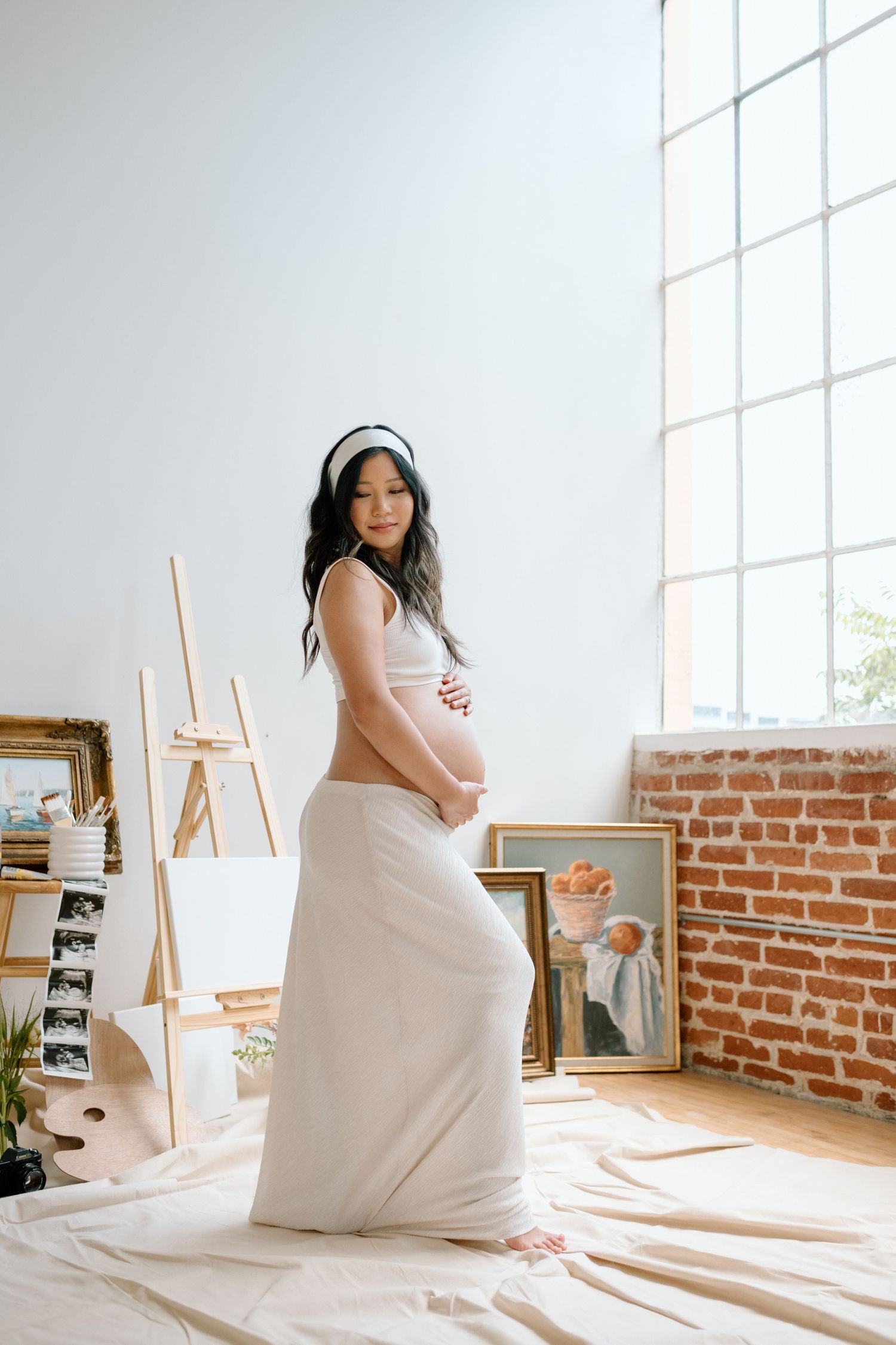 Pregnant woman stands among paintings during maternity photoshoot in a San Diego studio.